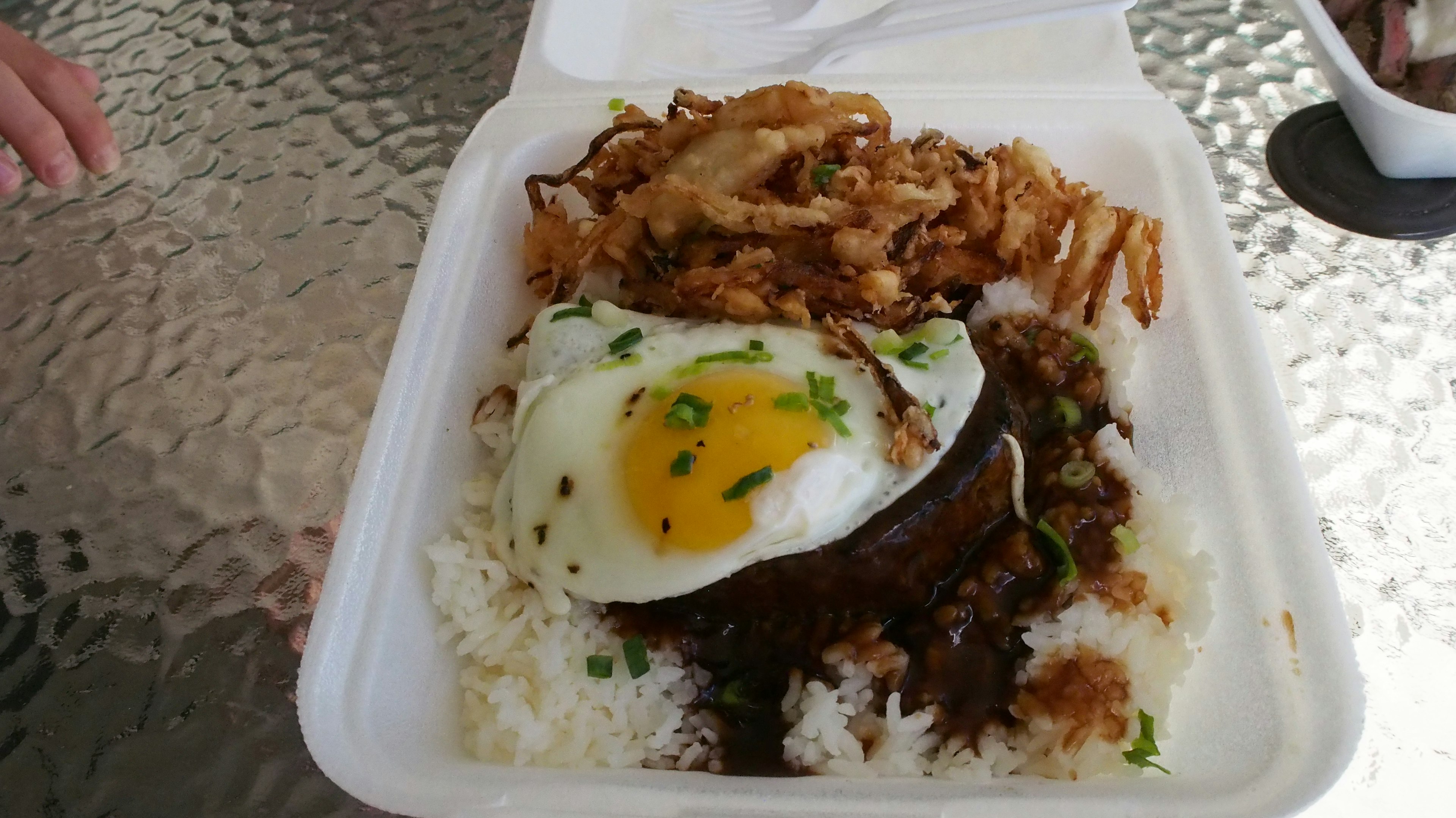 A dish served in a white container with rice topped with a fried egg and meat