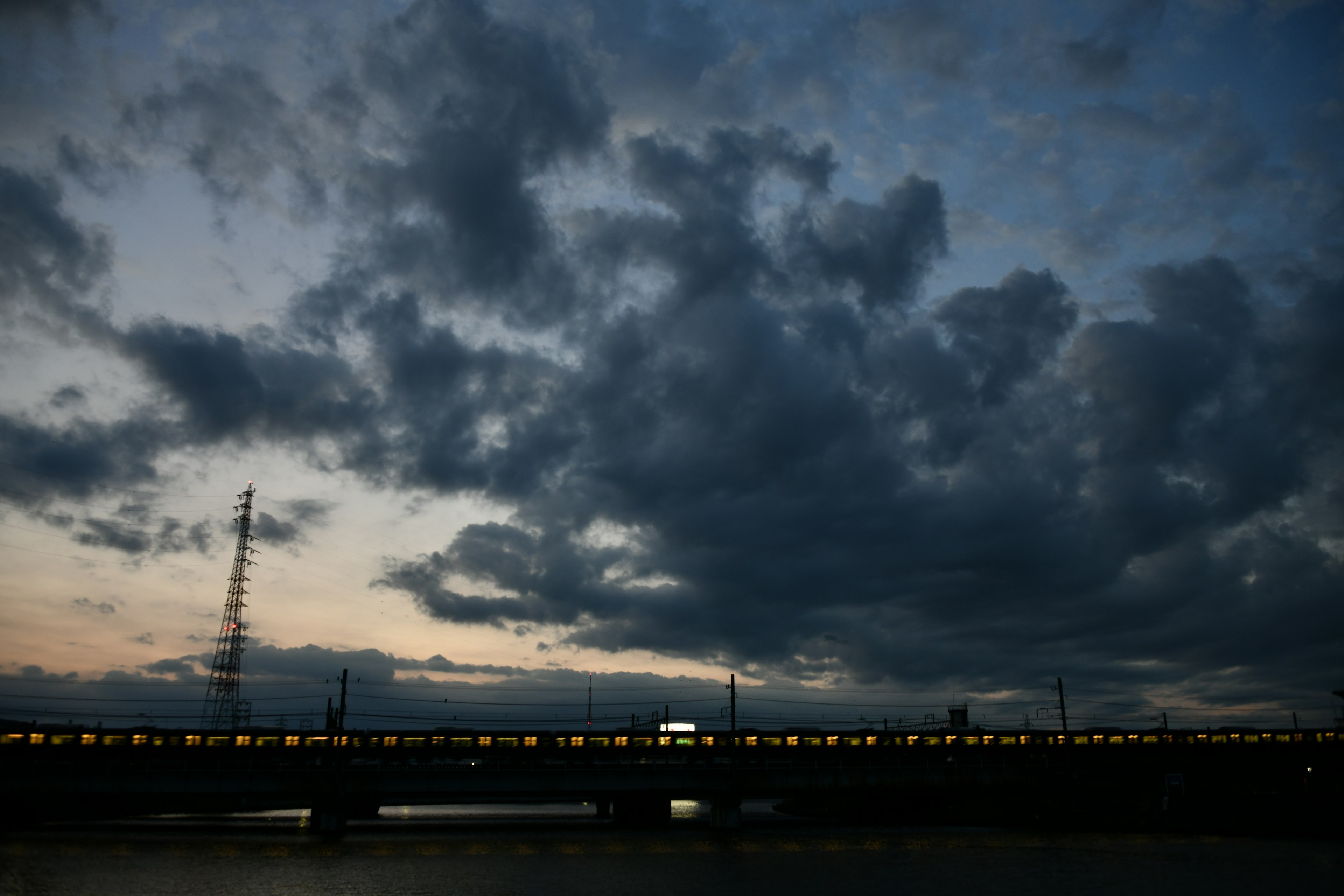 Dämmerungsszene mit einer Brücke und einem Zug unter dunklen Wolken und orangefarbener Beleuchtung