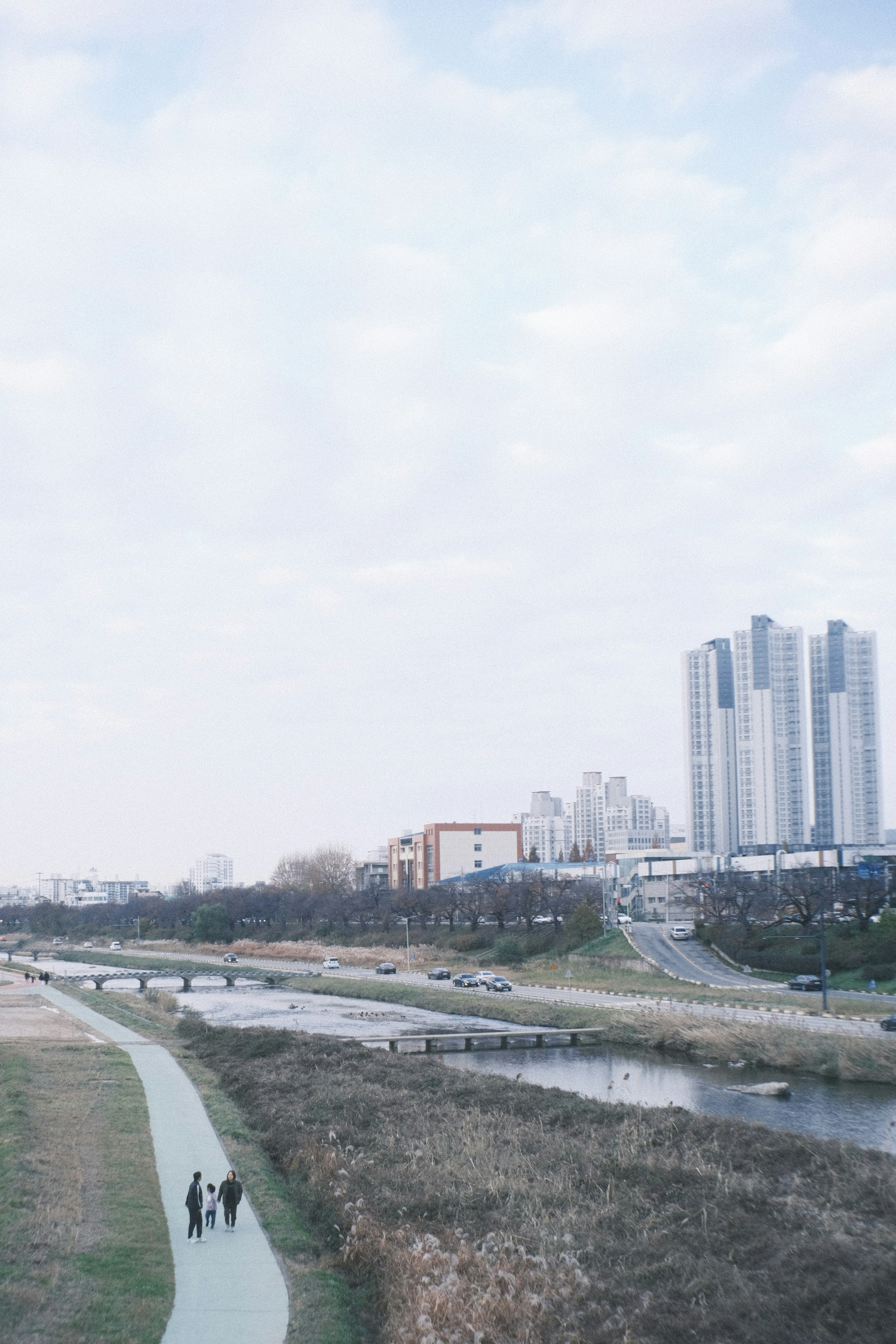 People walking along a riverside path with skyscrapers in the background