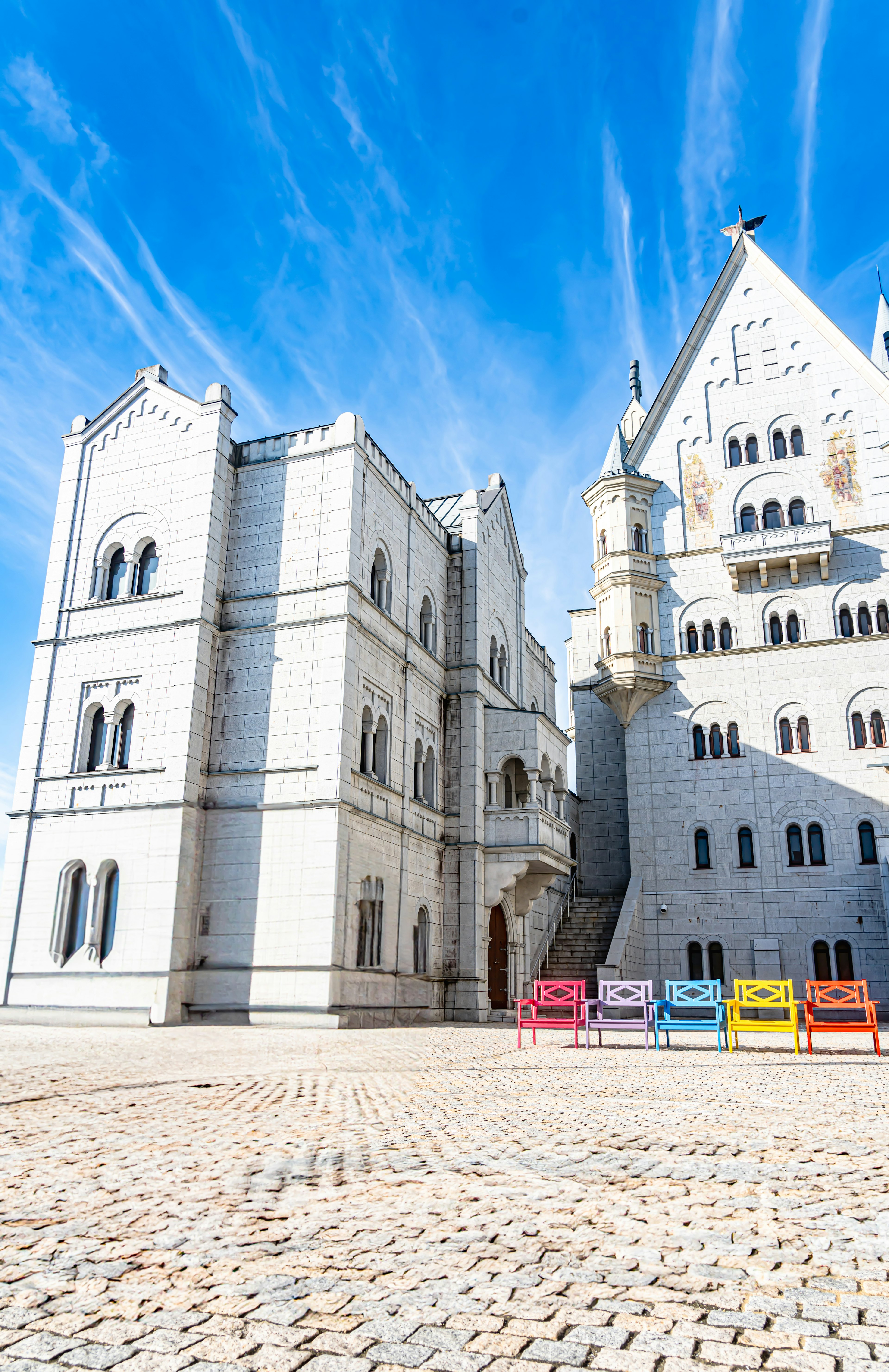 Un edificio blanco parecido a un castillo con sillas de colores dispuestas en la plaza