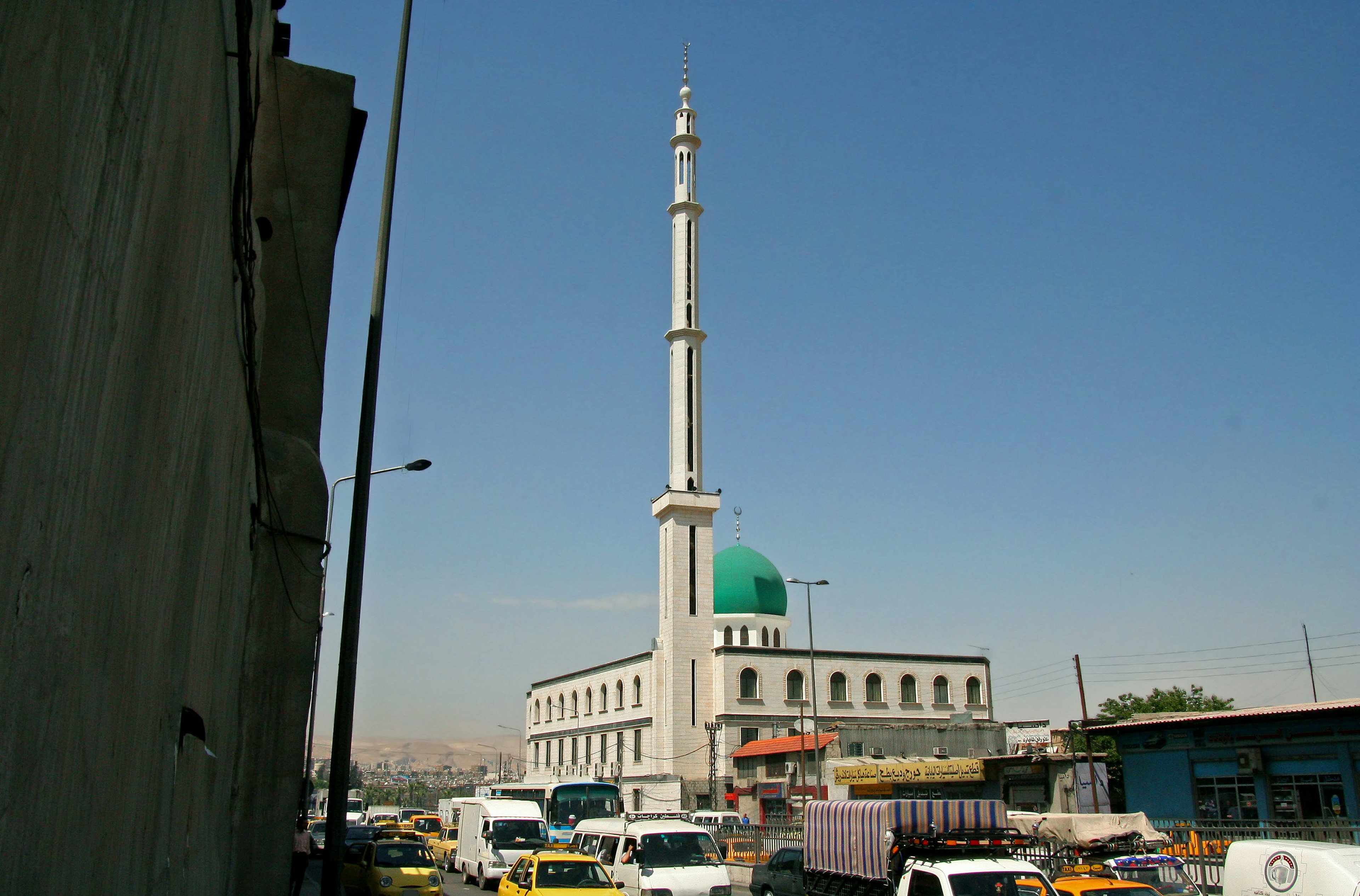 Mosque with a green dome and city traffic in the foreground