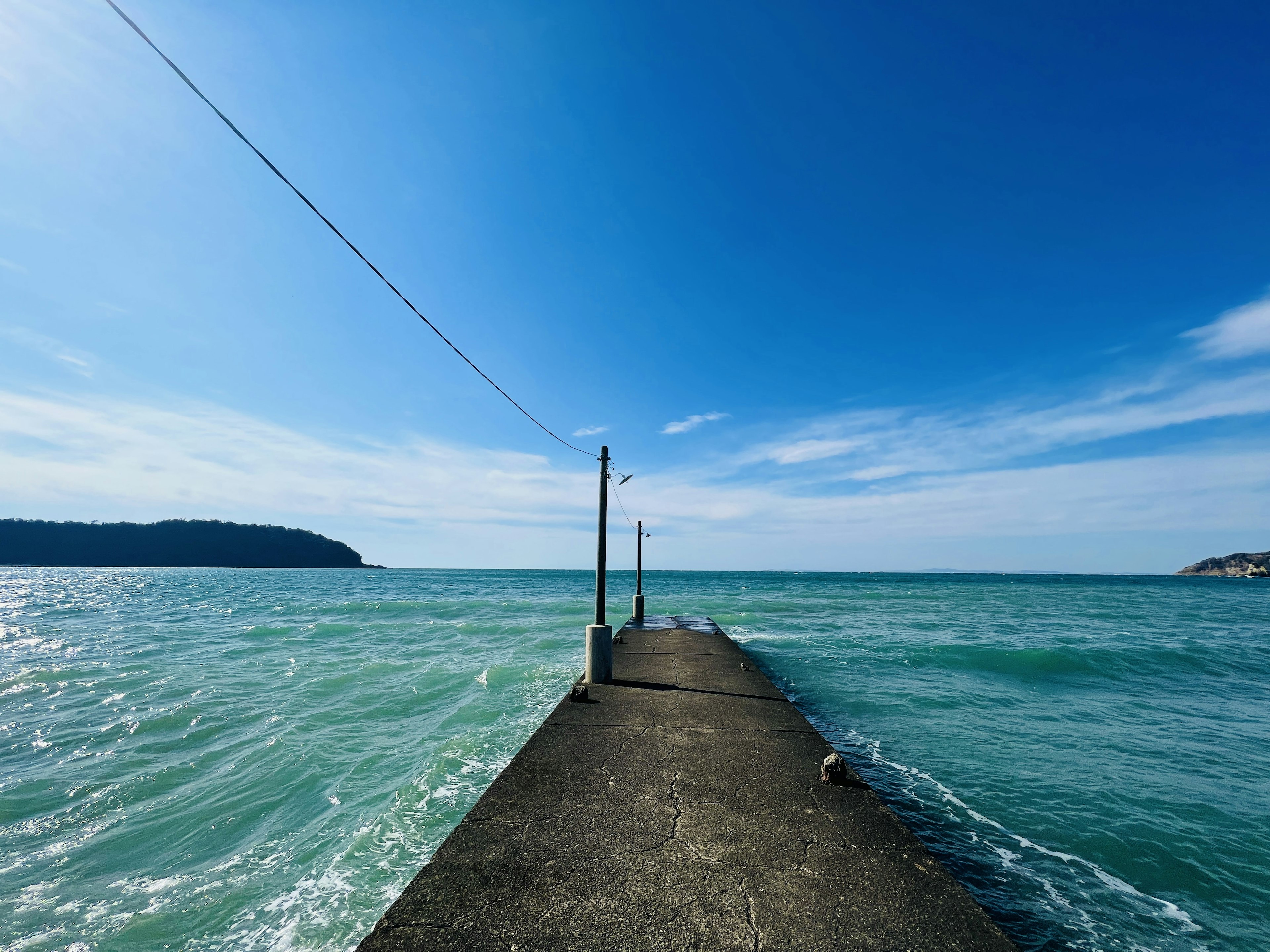 Betonpier, der in türkises Wasser unter einem klaren blauen Himmel ragt