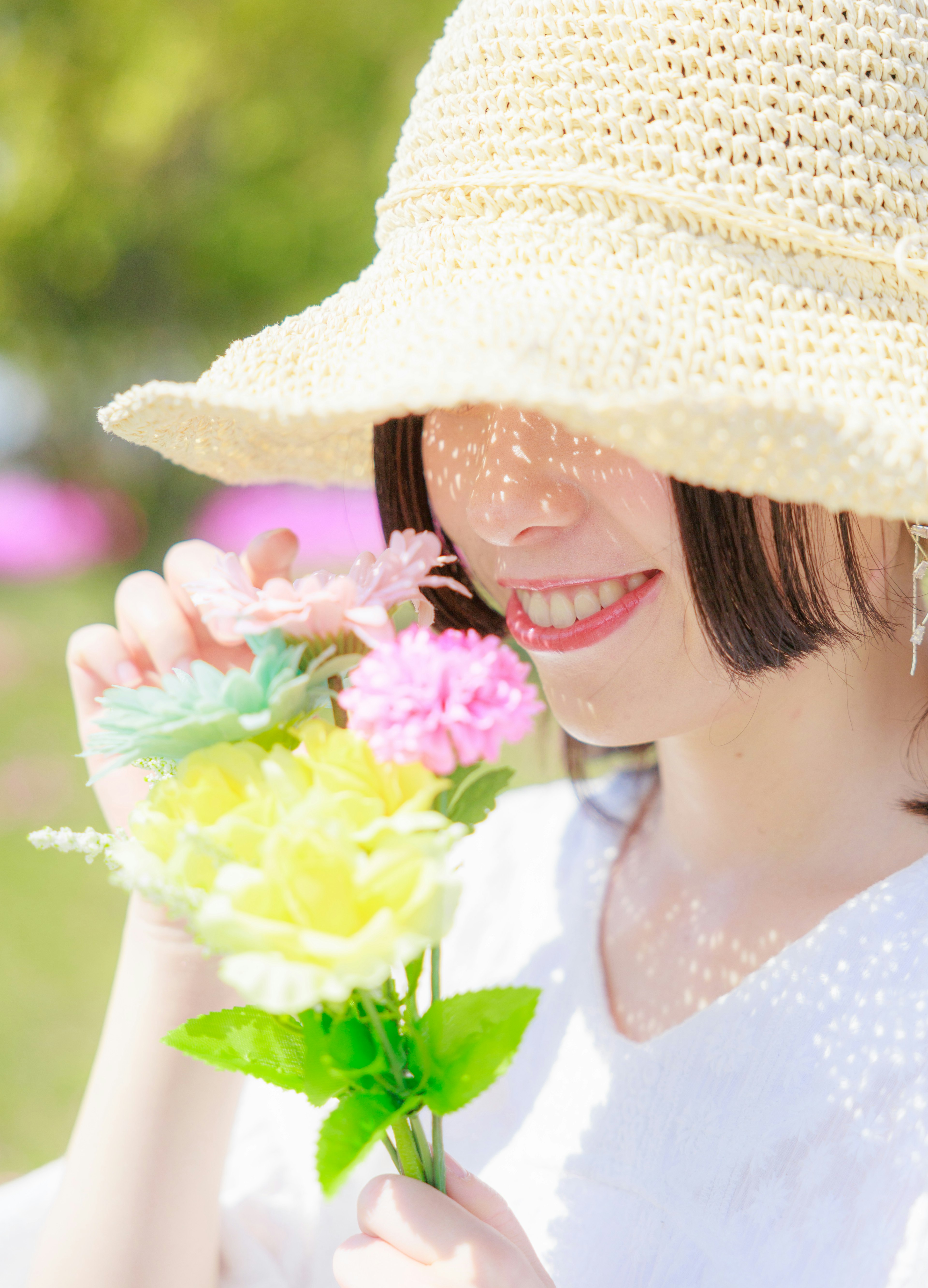 A woman wearing a straw hat holding colorful flowers and smiling