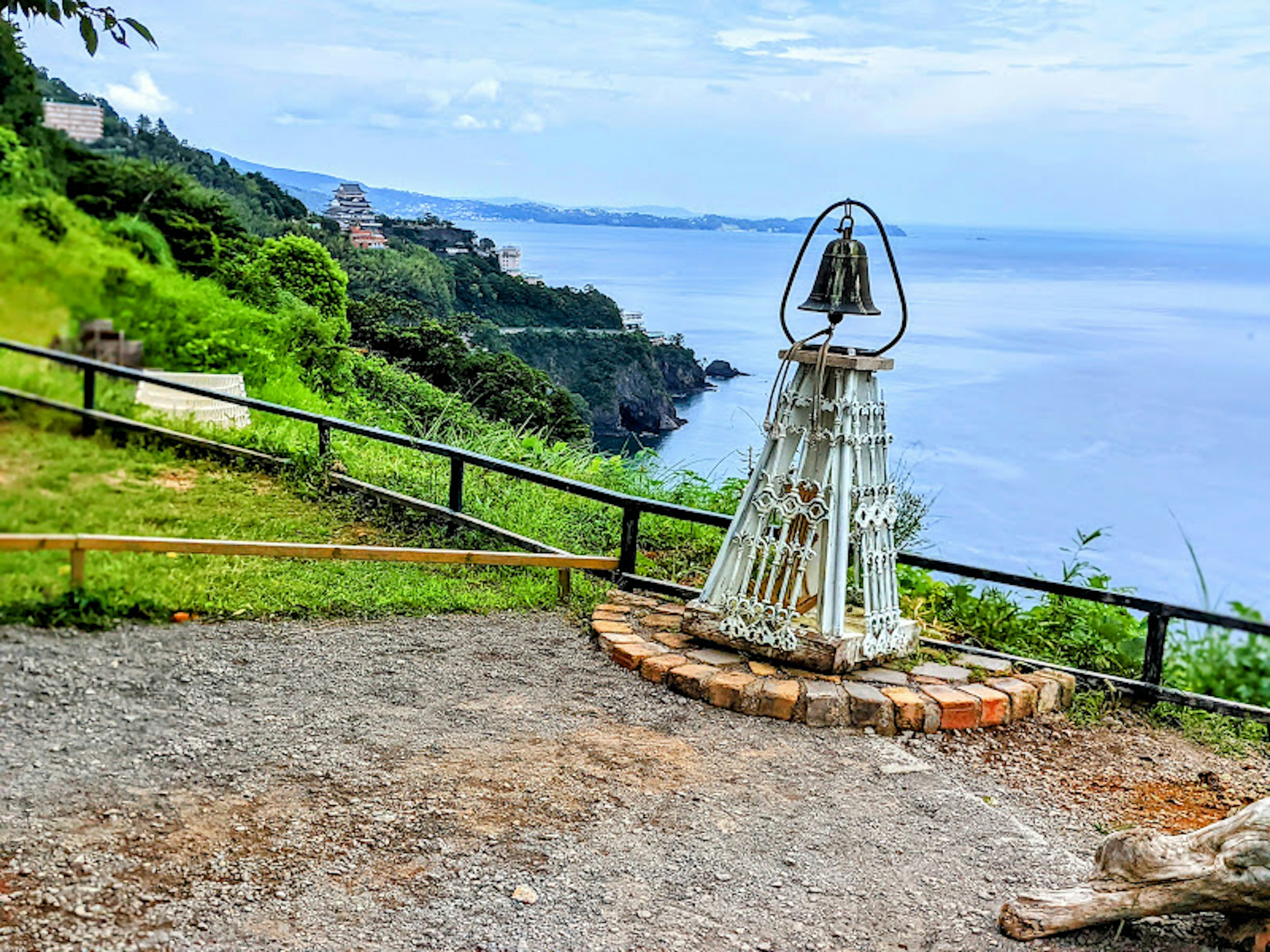 海を見下ろす丘の上にある鐘のモニュメントと緑の風景