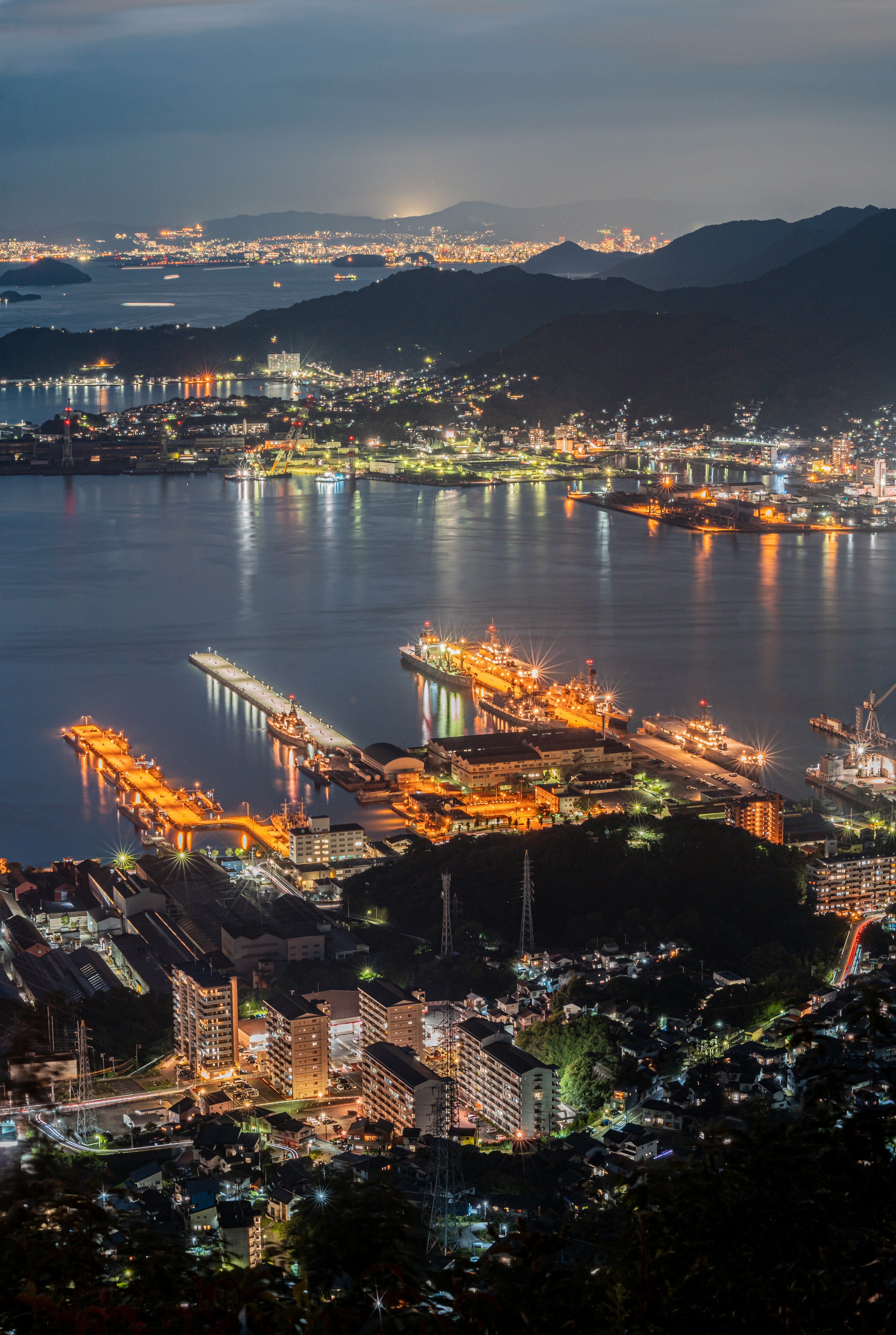 夜景の港町の空撮　明るい灯りが水面に反射　山々と都市が広がる