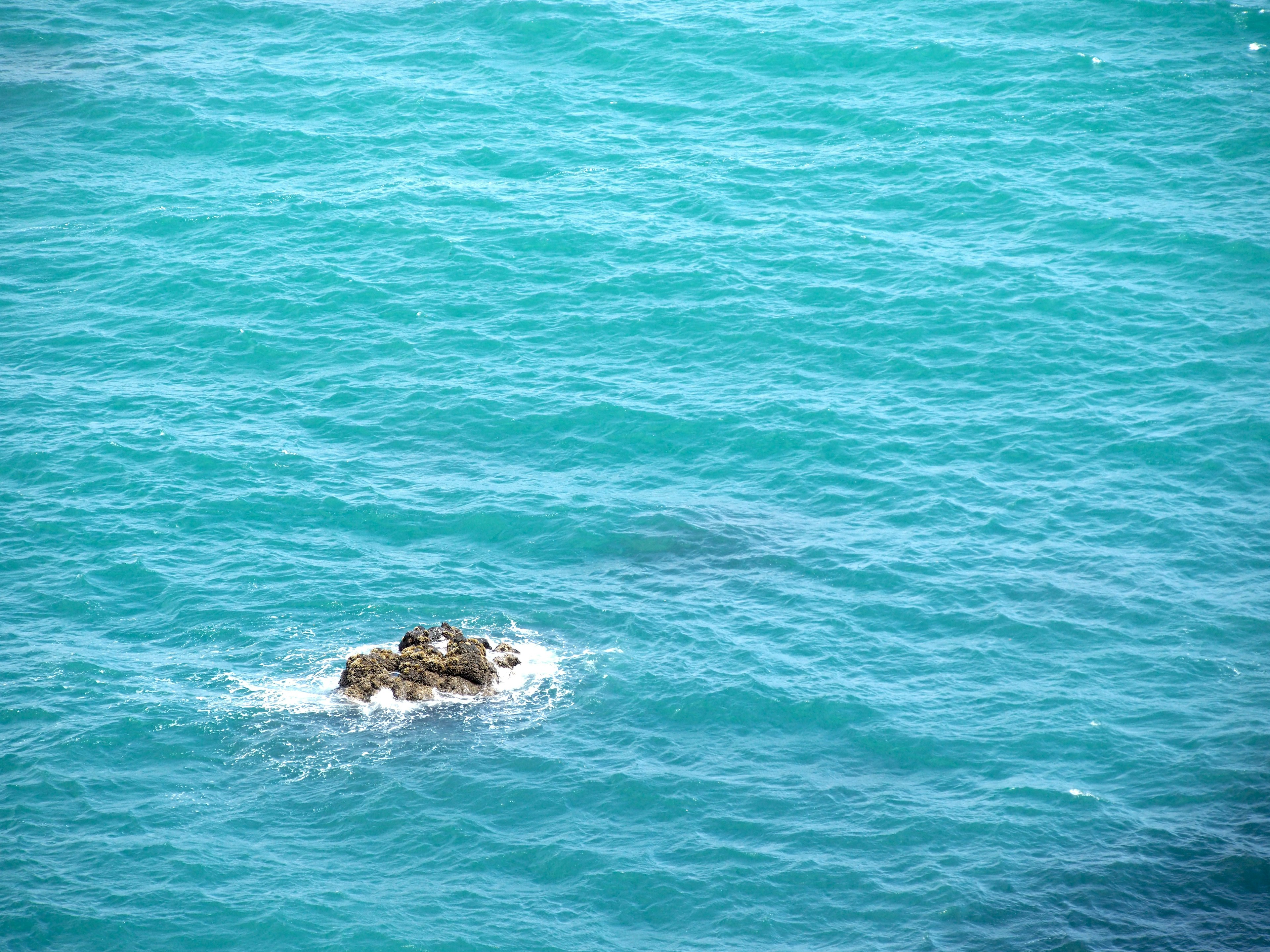 Ein kleiner Felsen umgeben von türkisfarbenem Wasser im Ozean