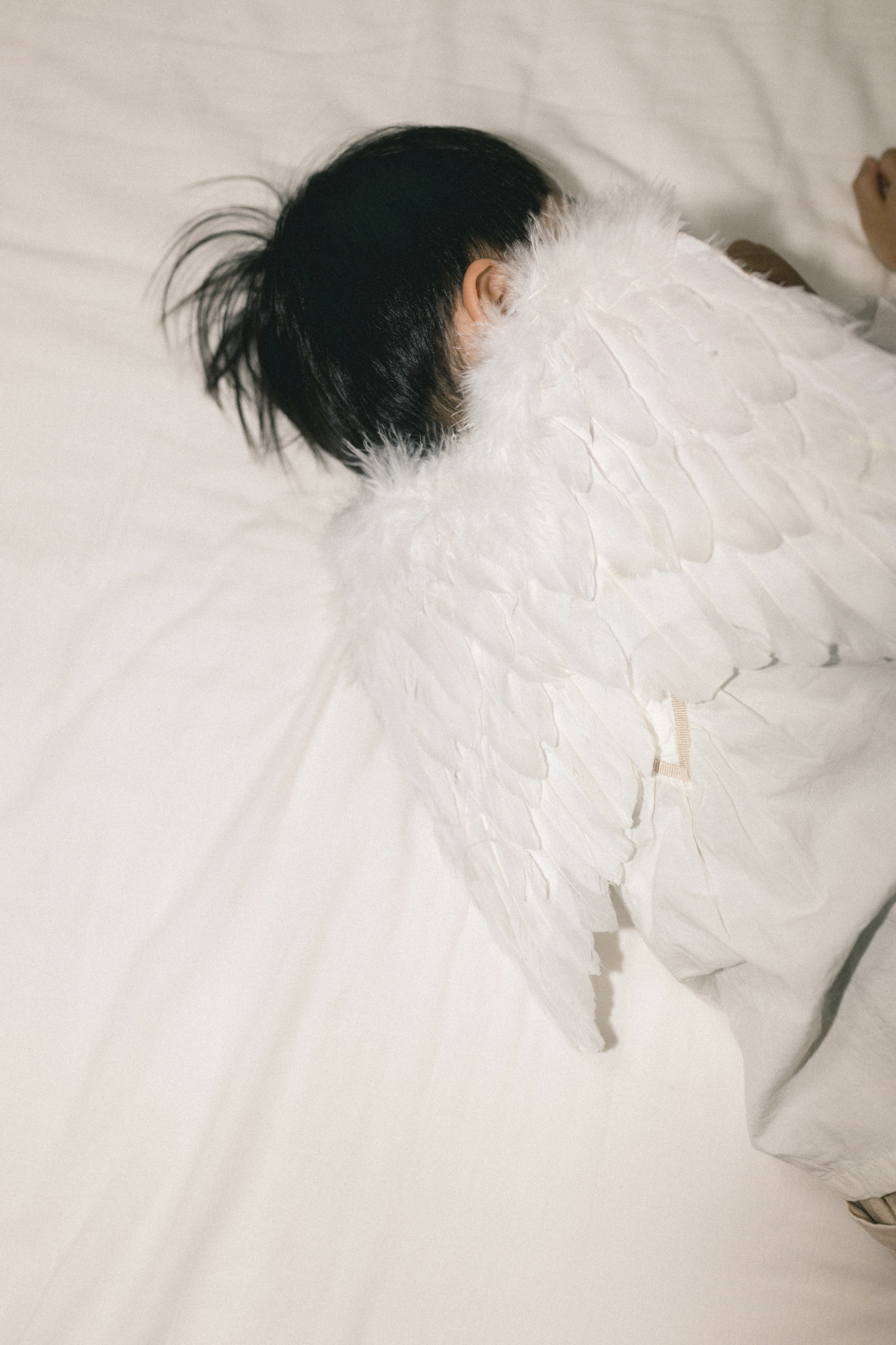 A child with angel wings sleeping on a white bed