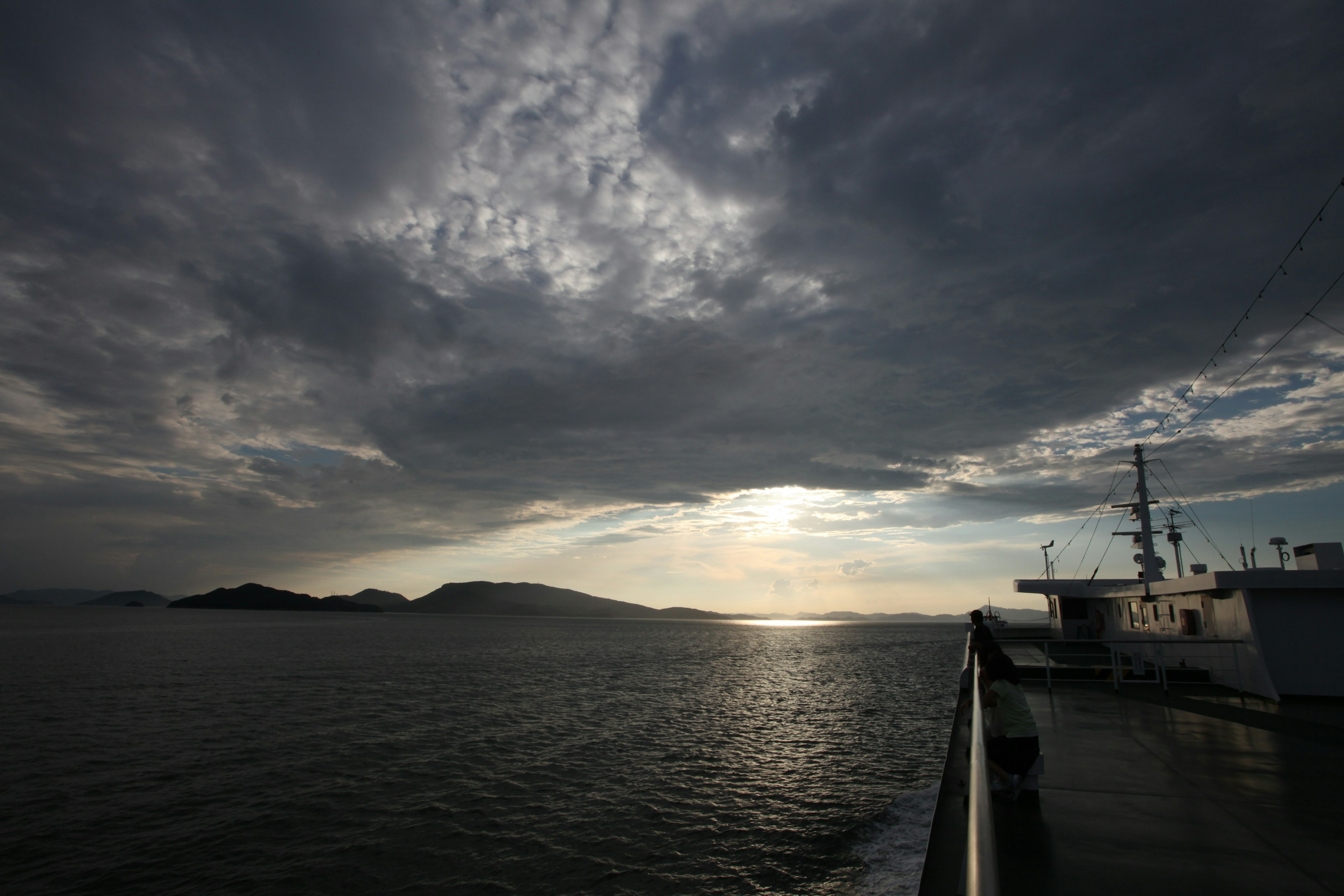 船の横から見える海と島の景色 曇り空と光が差し込む水面