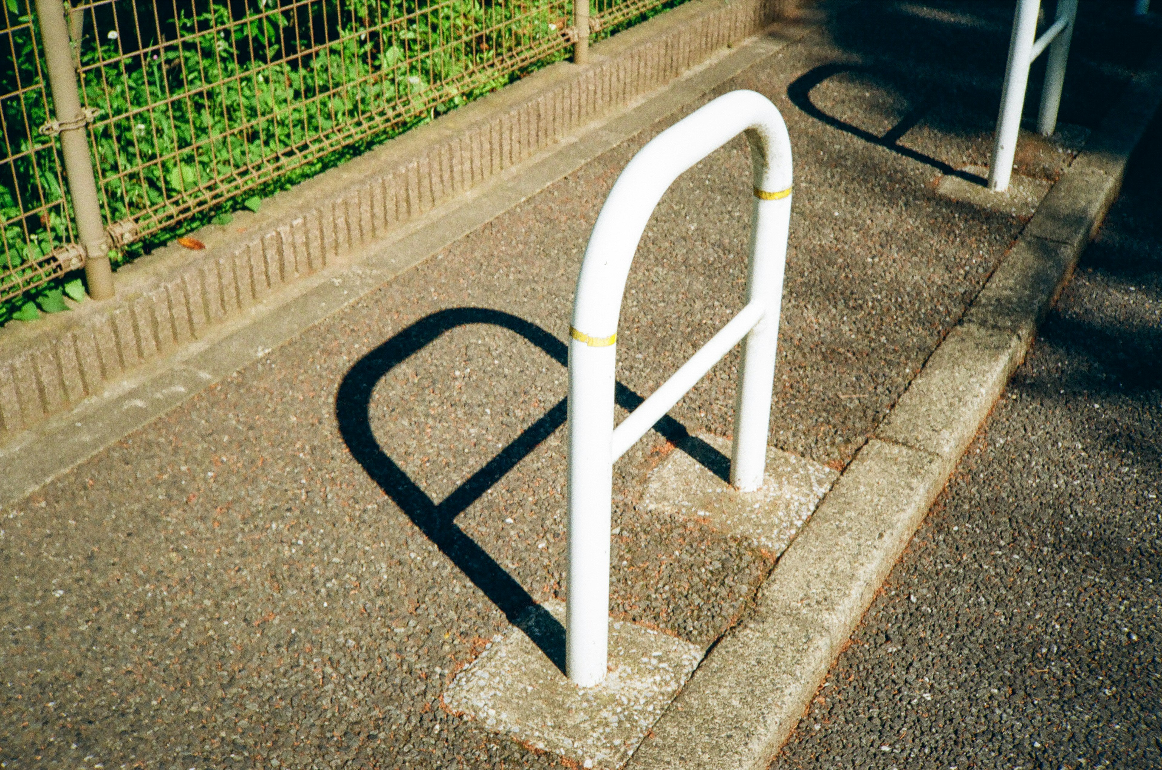 A white bicycle rack casting a shadow on the pavement