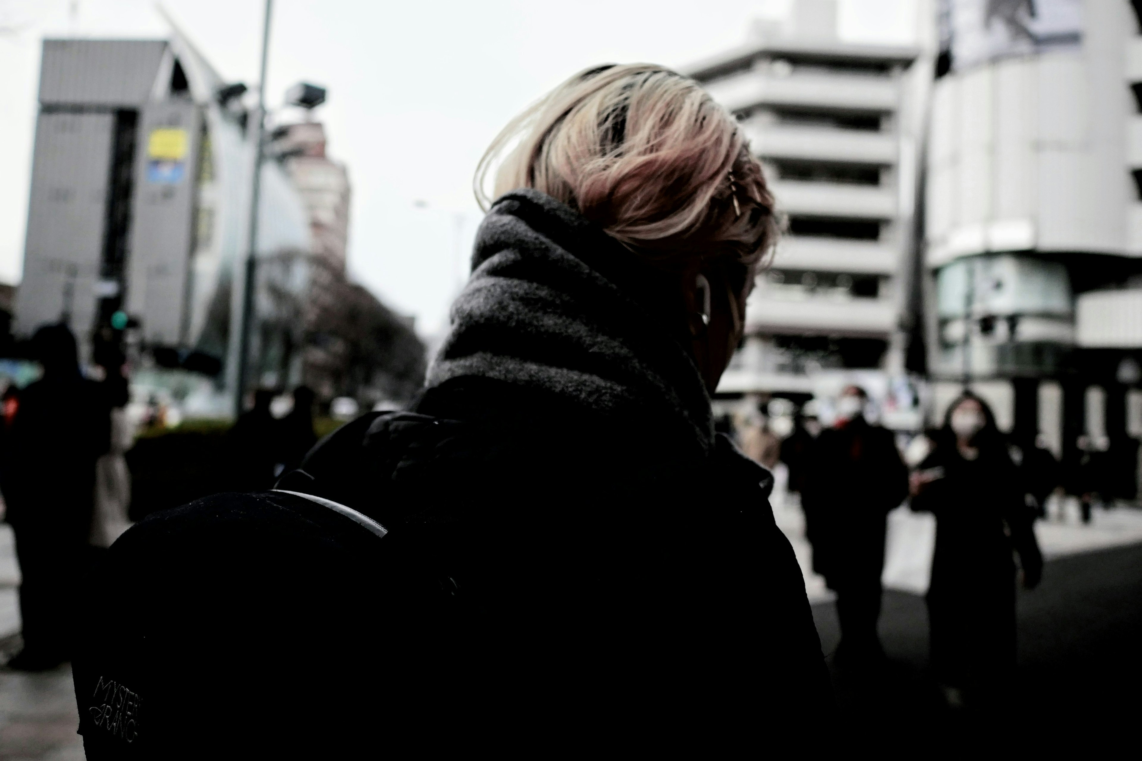 Personne aux cheveux clairs vue de dos dans une rue urbaine sombre avec des immeubles de grande hauteur