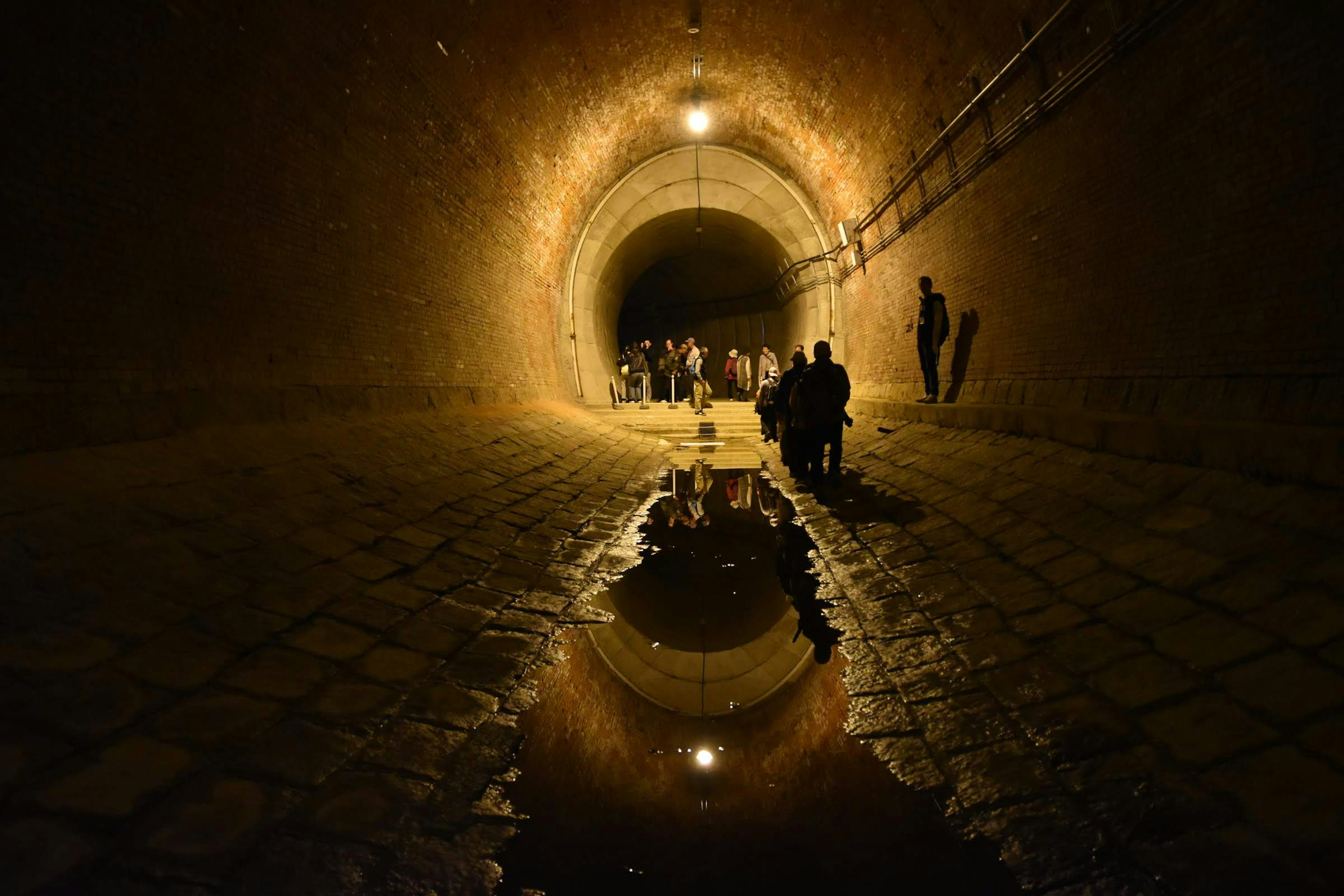 People gathered in a dark tunnel with a reflection in a puddle