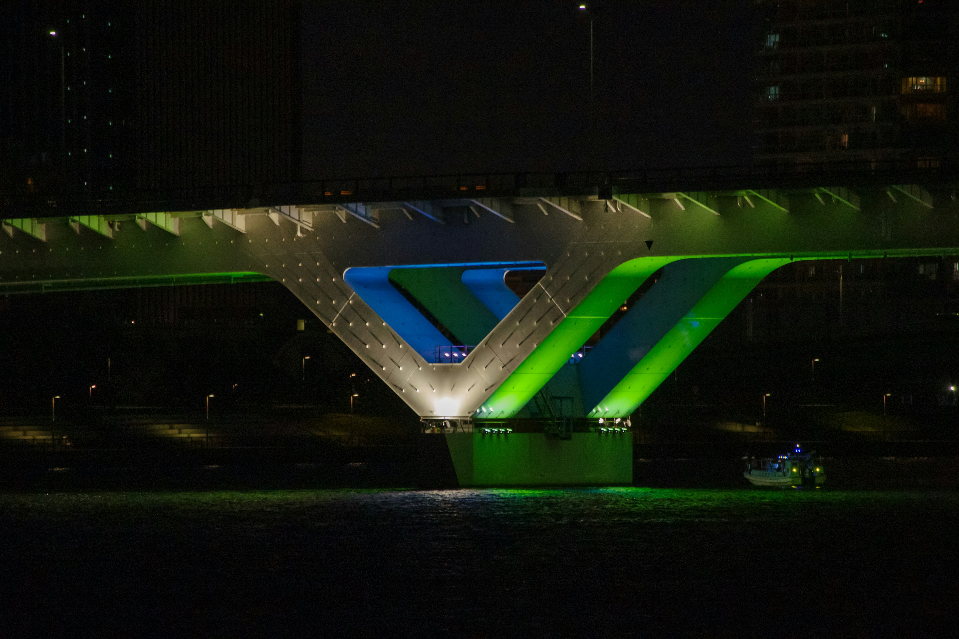 Modern bridge structure illuminated with green and blue lights at night