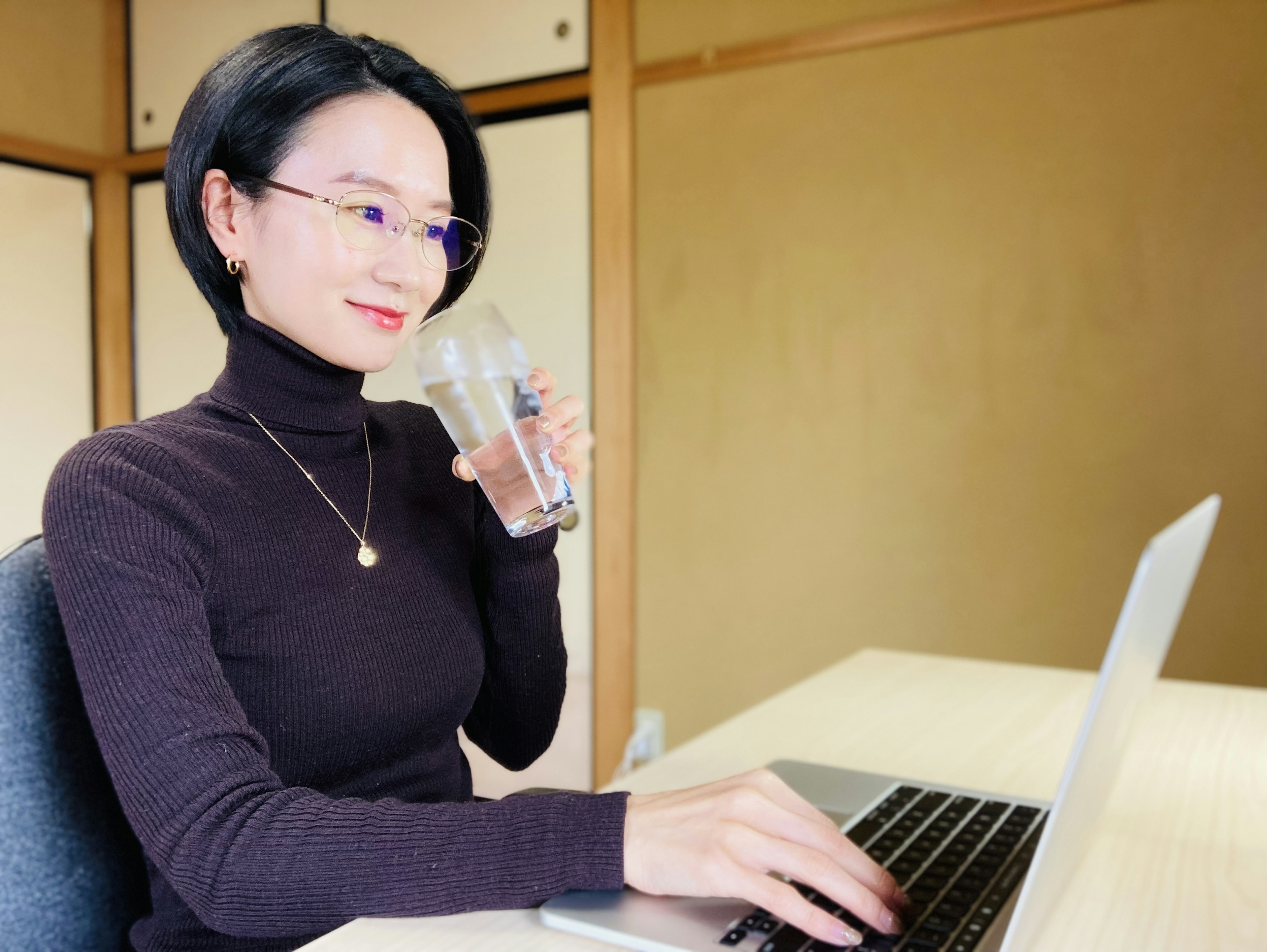 女性が水を飲みながらノートパソコンで作業しているシーン