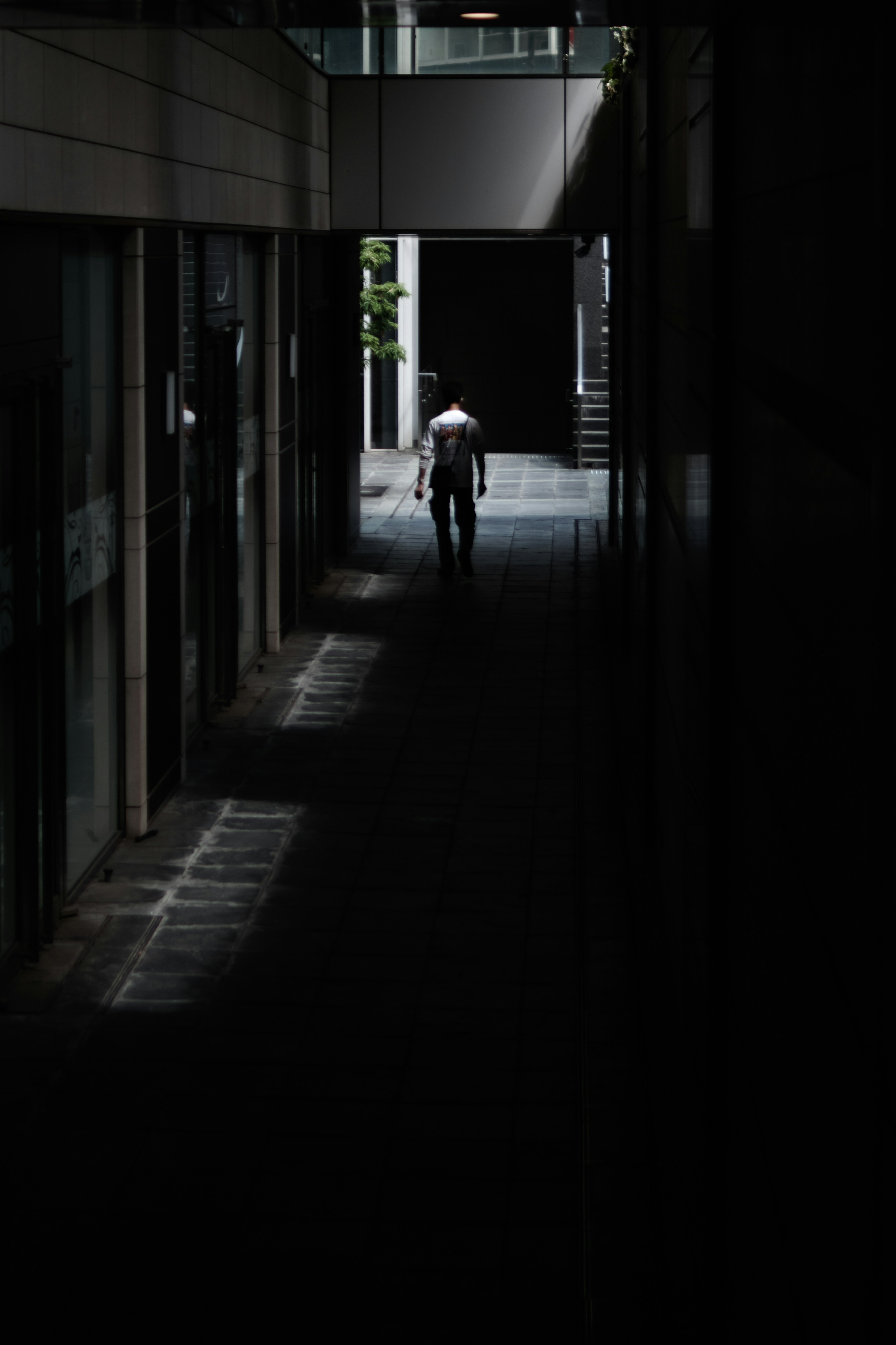 A figure walking through a dimly lit corridor with stark light and shadow contrasts