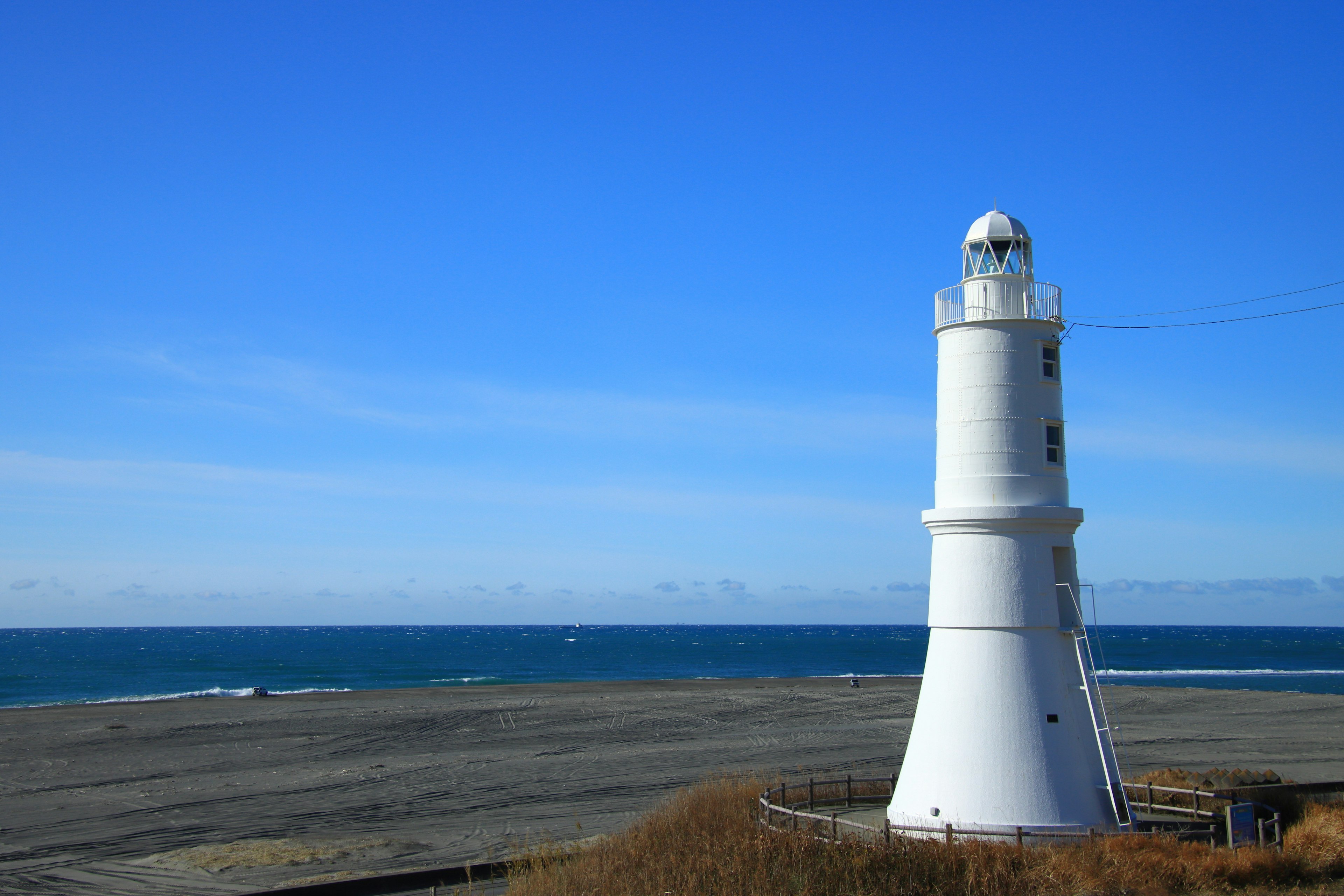 Faro blanco de pie contra un cielo azul y el océano