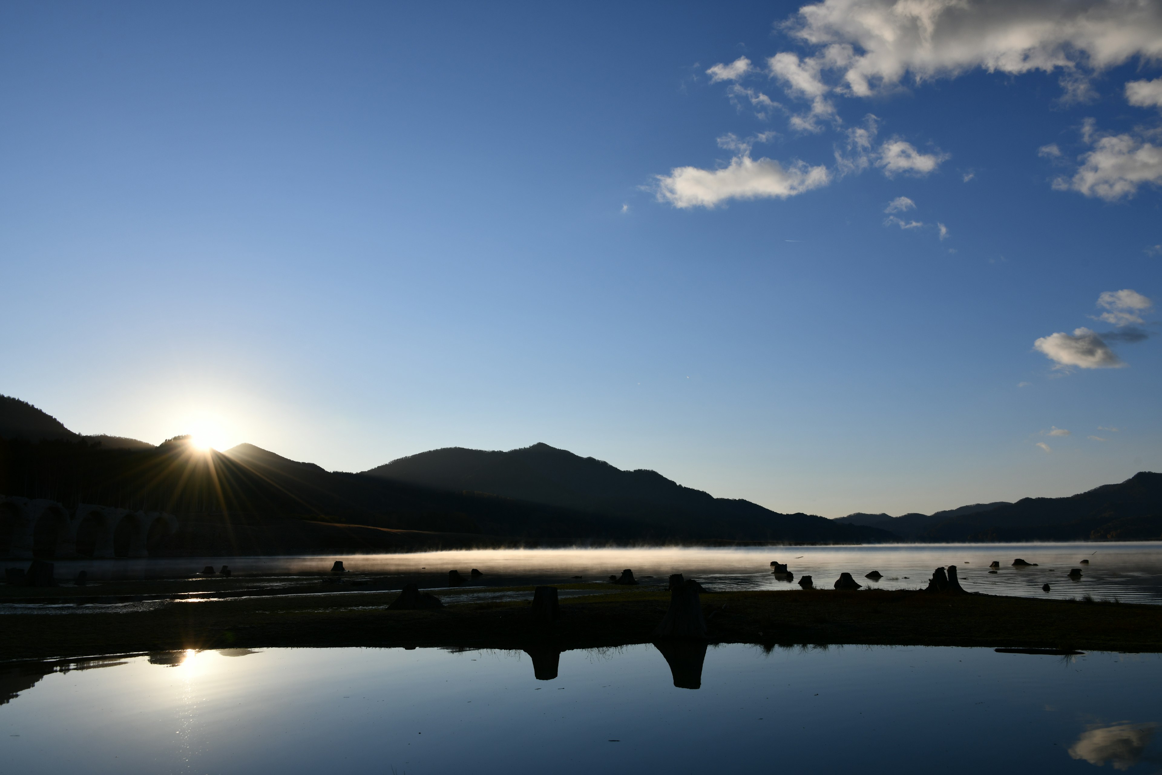 静かな湖と山々のシルエットを背景にした日の出の風景