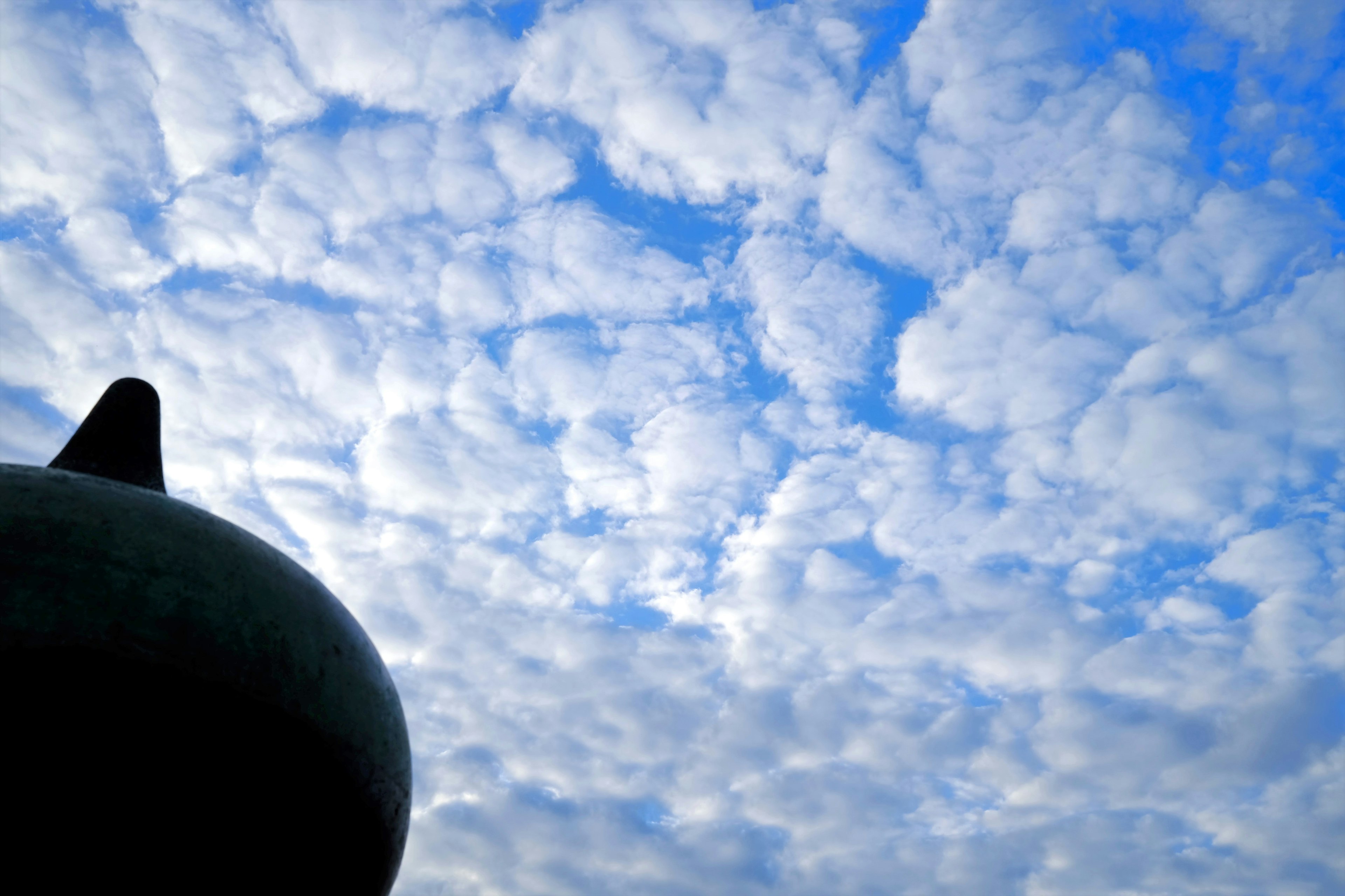 Silhouette di un oggetto nero contro un cielo blu pieno di nuvole bianche