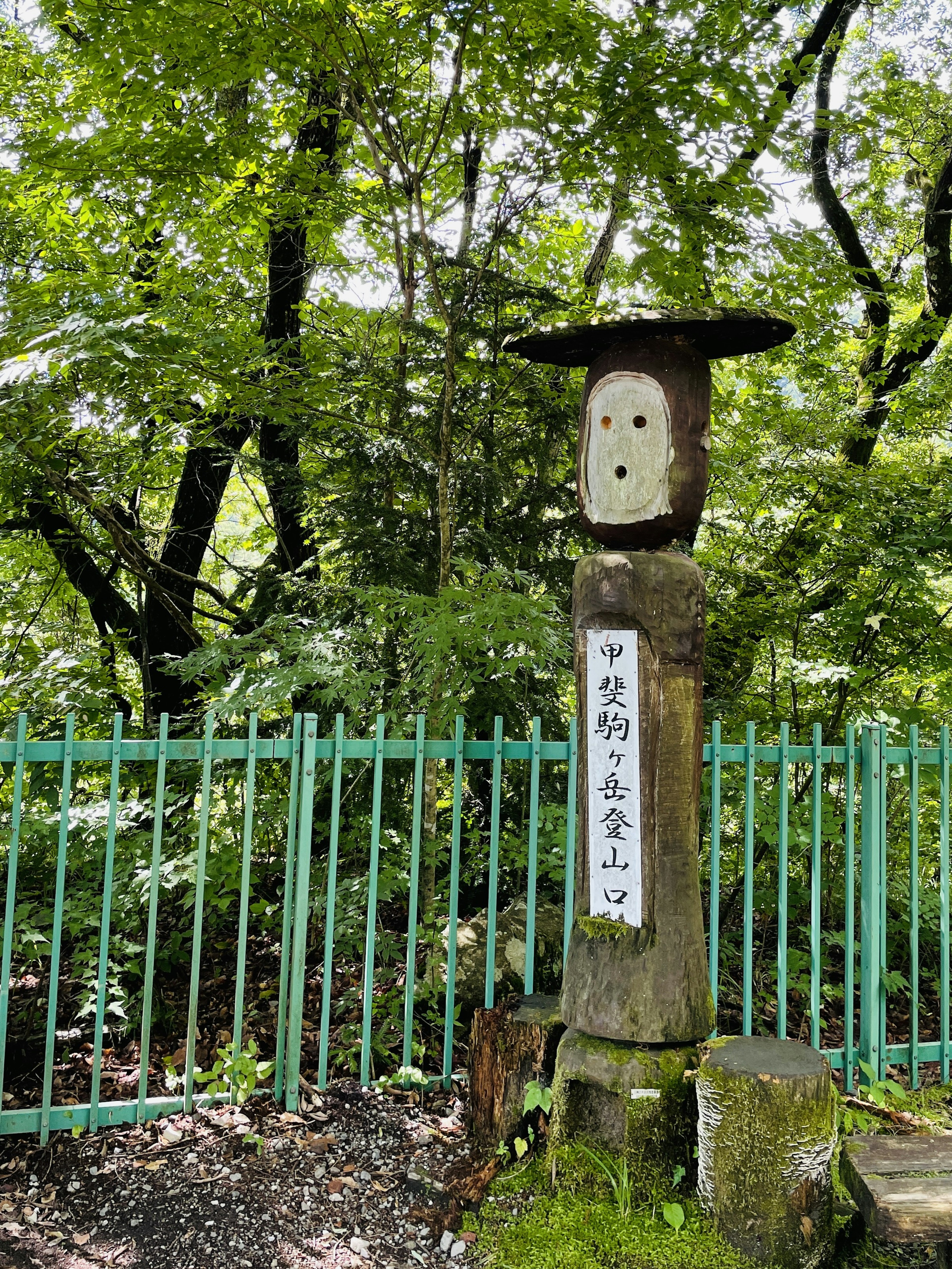 Statua in legno in una foresta con iscrizione giapponese su una targa