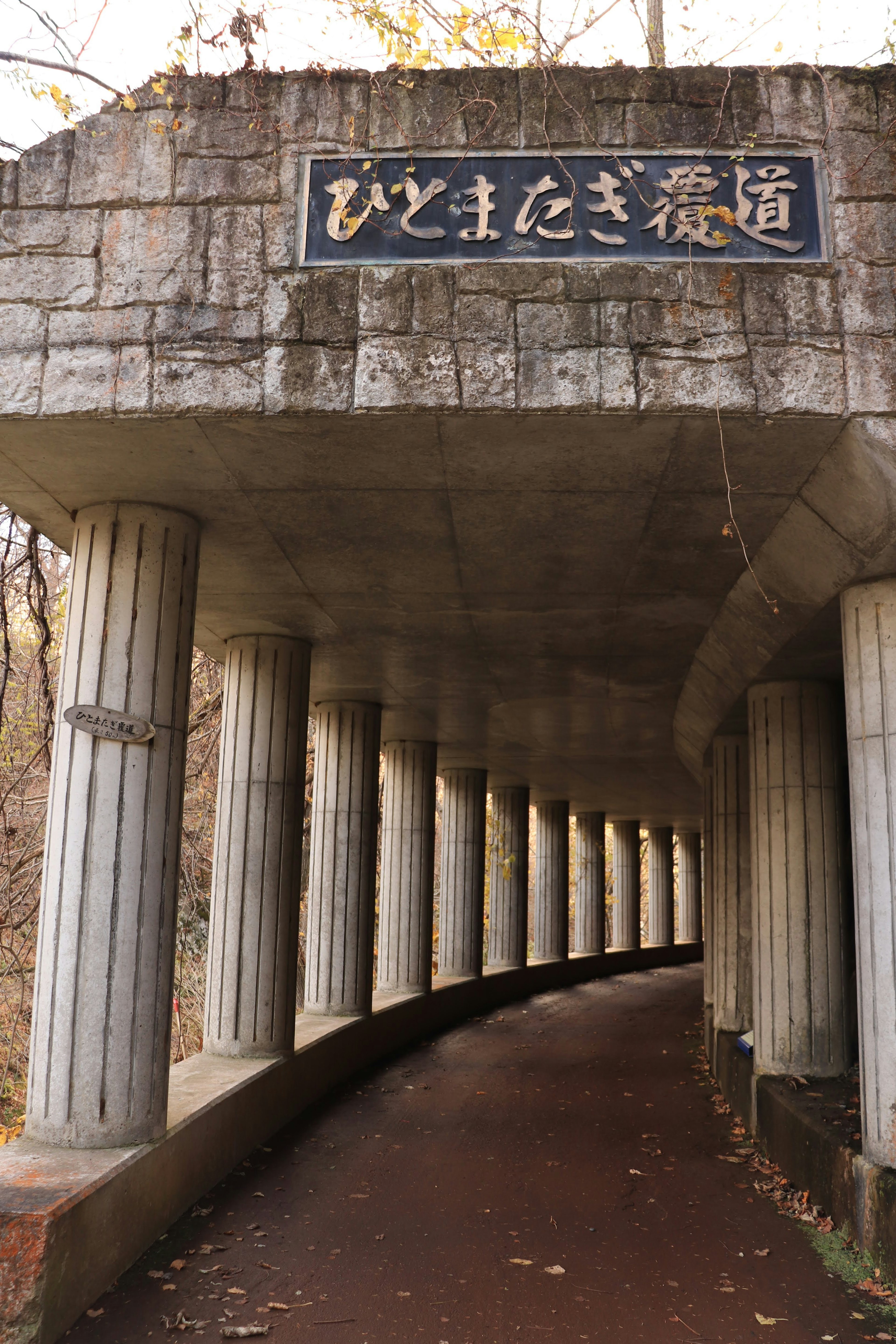 Camino curvado de concreto con columnas y letrero en japonés arriba