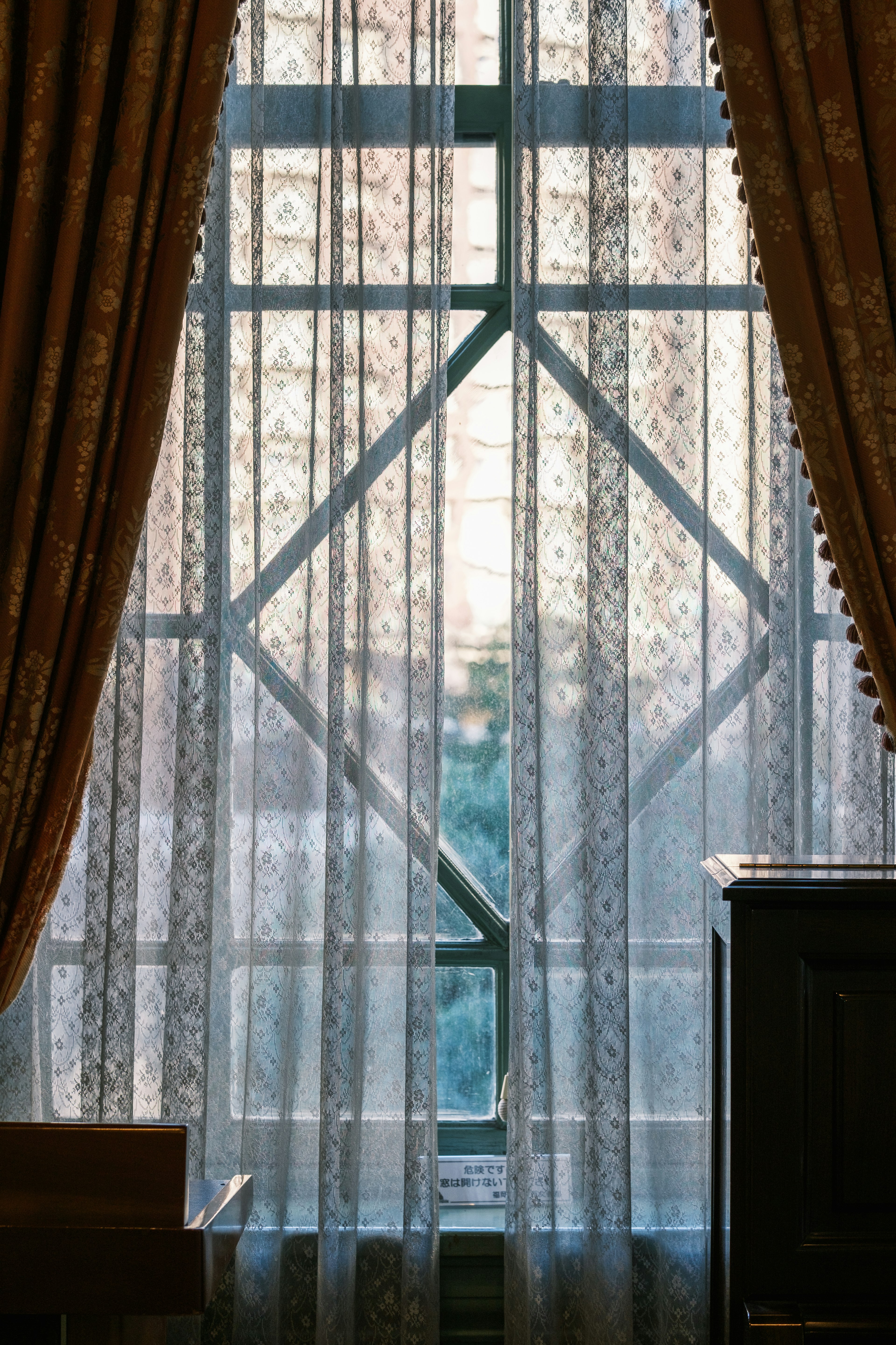 Window view through sheer curtains Soft light filtering through sheer lace curtains with rich drapery