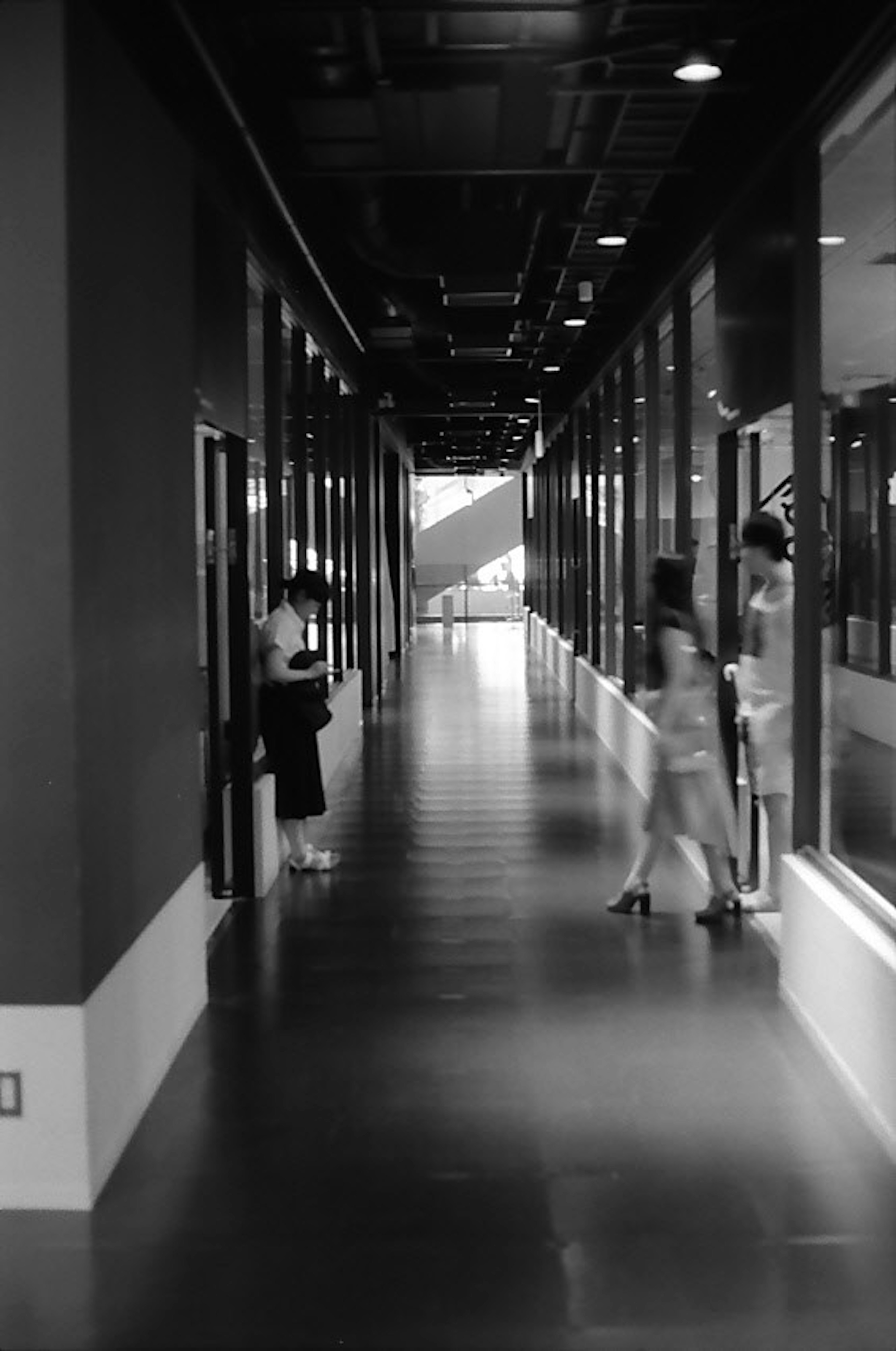 Couloir long en noir et blanc avec des femmes et des portes en verre