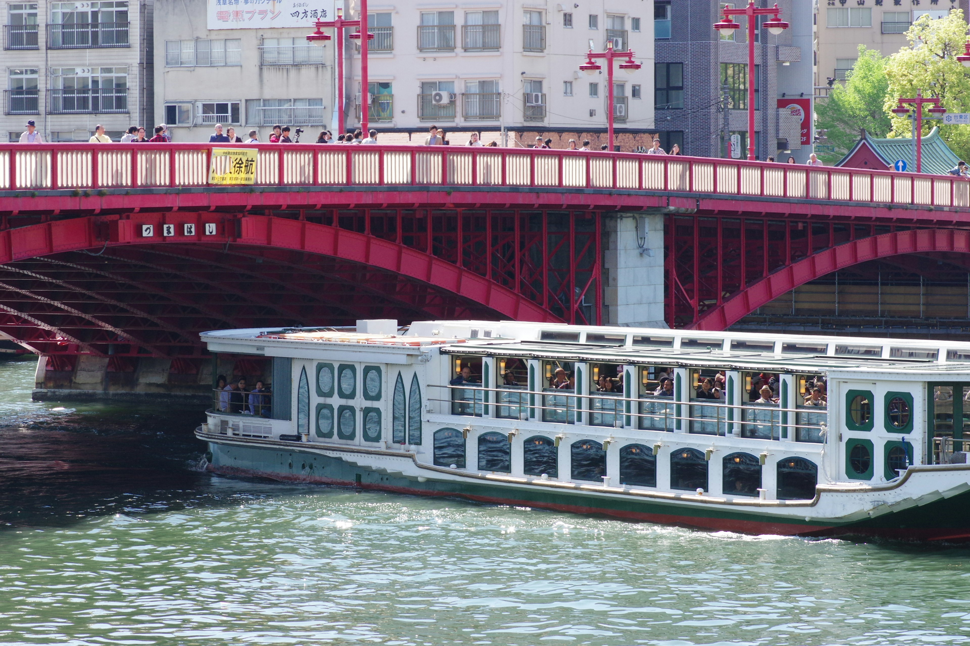 Barco turístico pasando por debajo de un puente rojo con paisaje fluvial