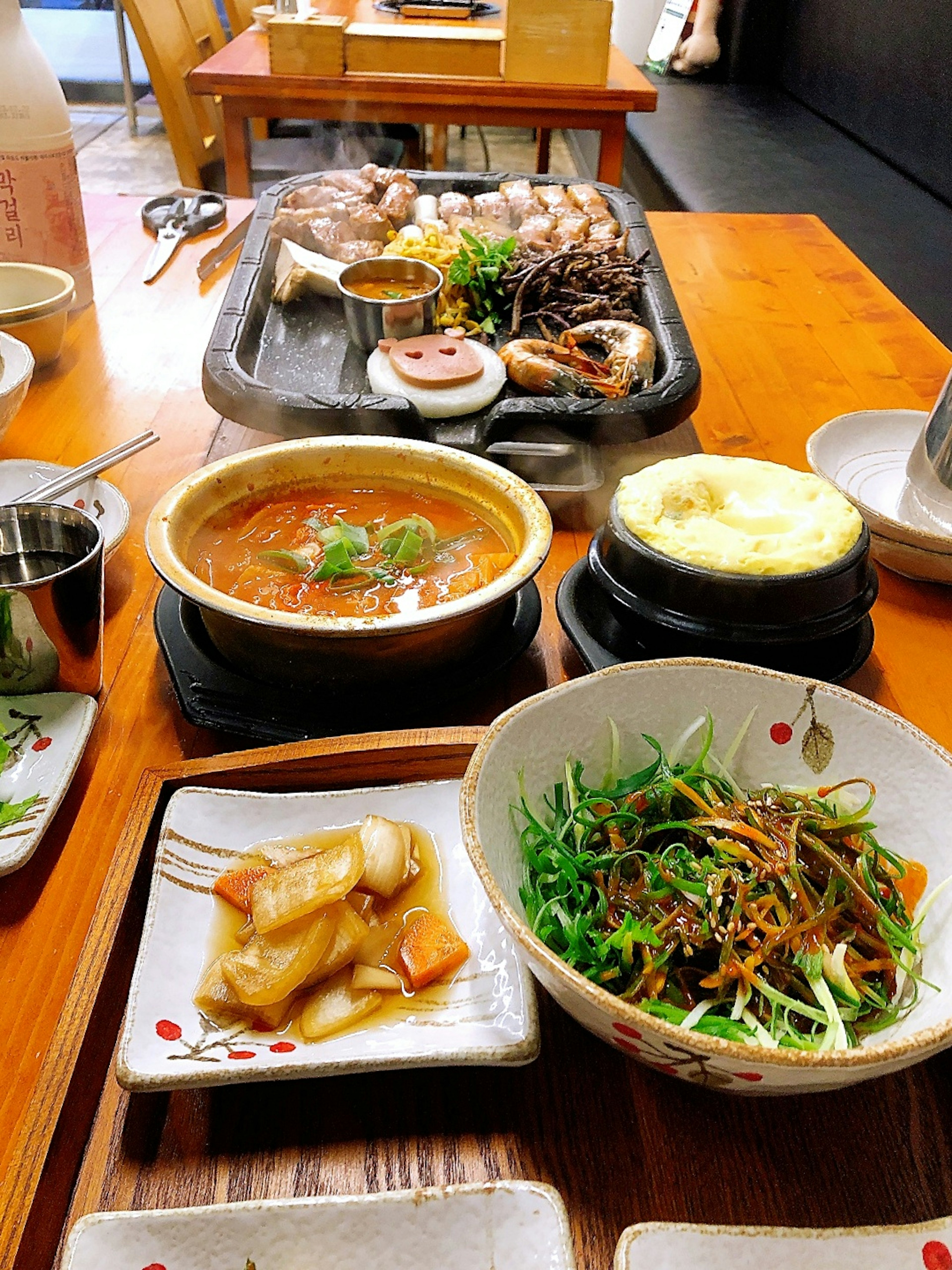 한국 요리 테이블 세팅으로 구운 고기, 국물, 샐러드, 김치가 놓여 있다