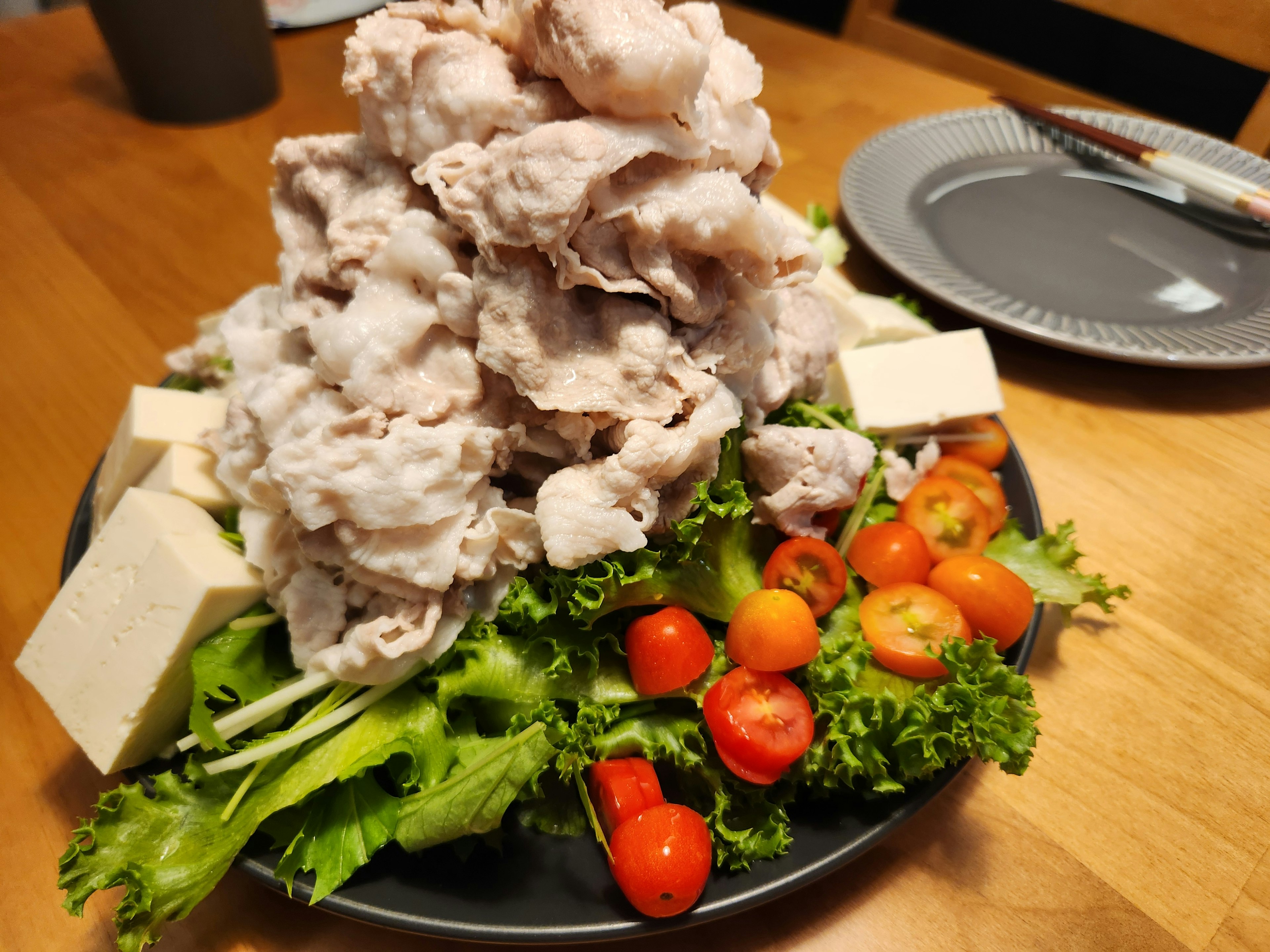 盛り付けられた新鮮な野菜と豆腐の上に山盛りの肉が載った料理