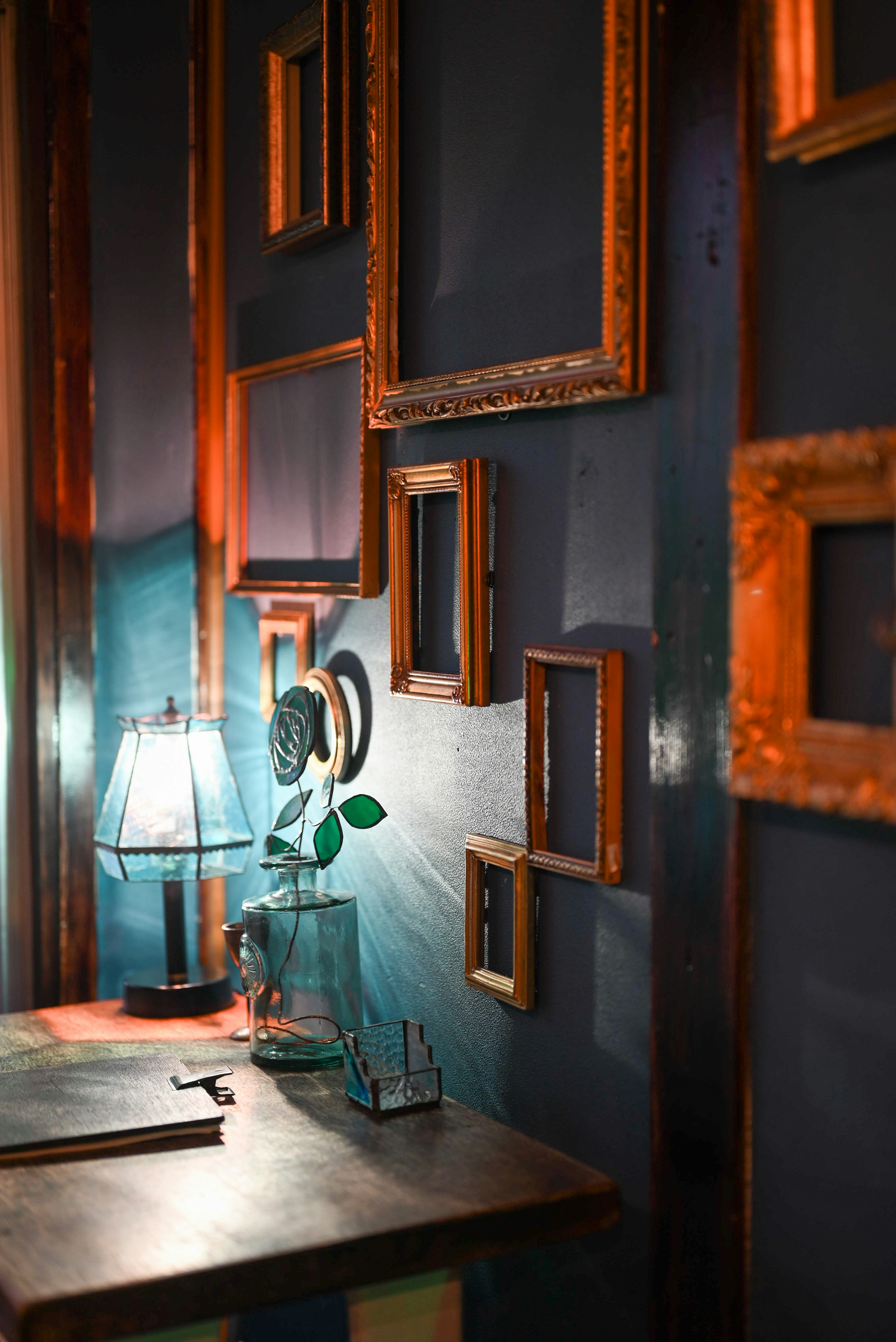 Corner of a room with blue walls adorned with golden frames Table with a lamp and a plant