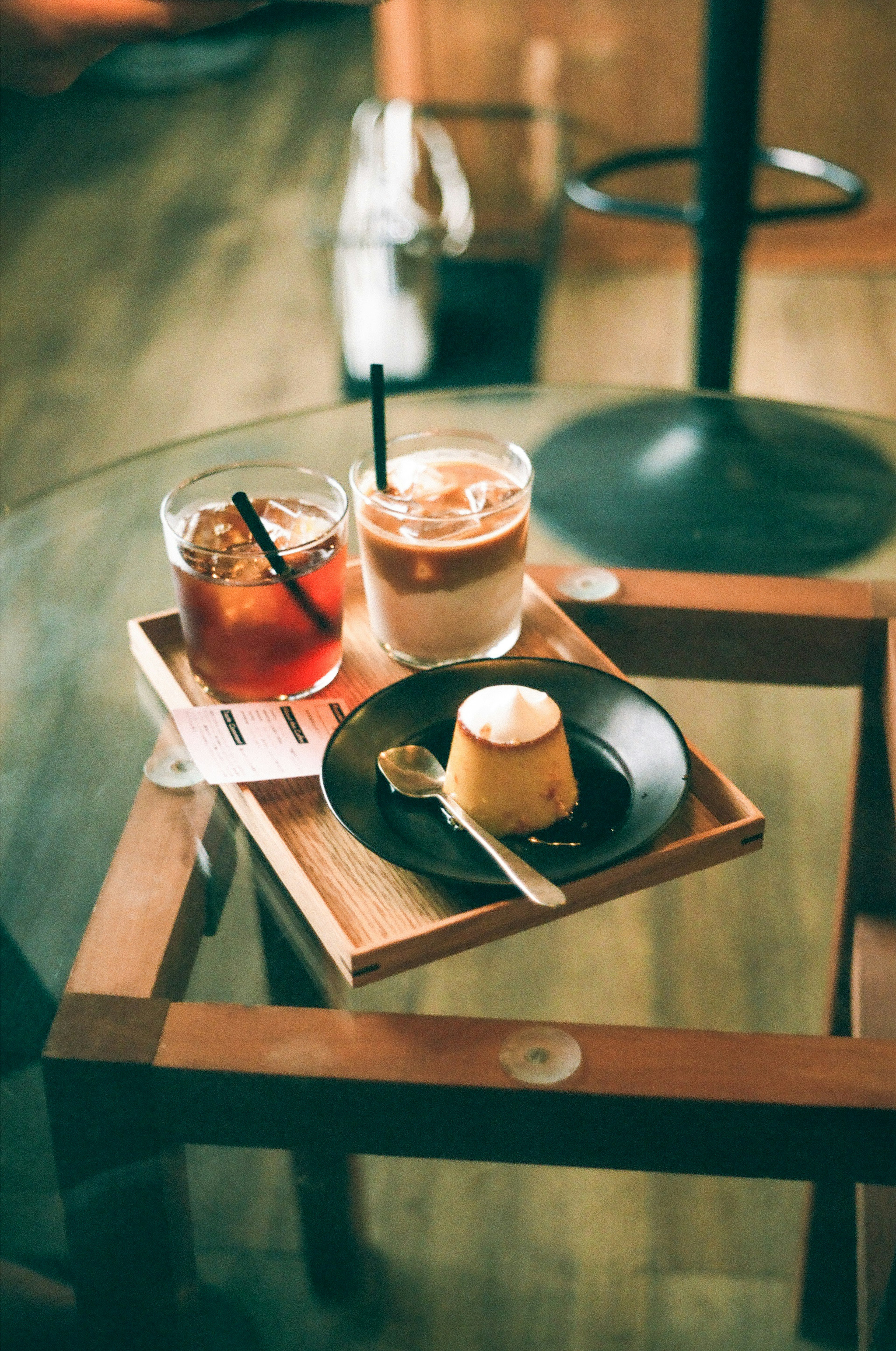 Zwei Gläser Eiskaffee und Tee mit einem Pudding auf einem Holztablett