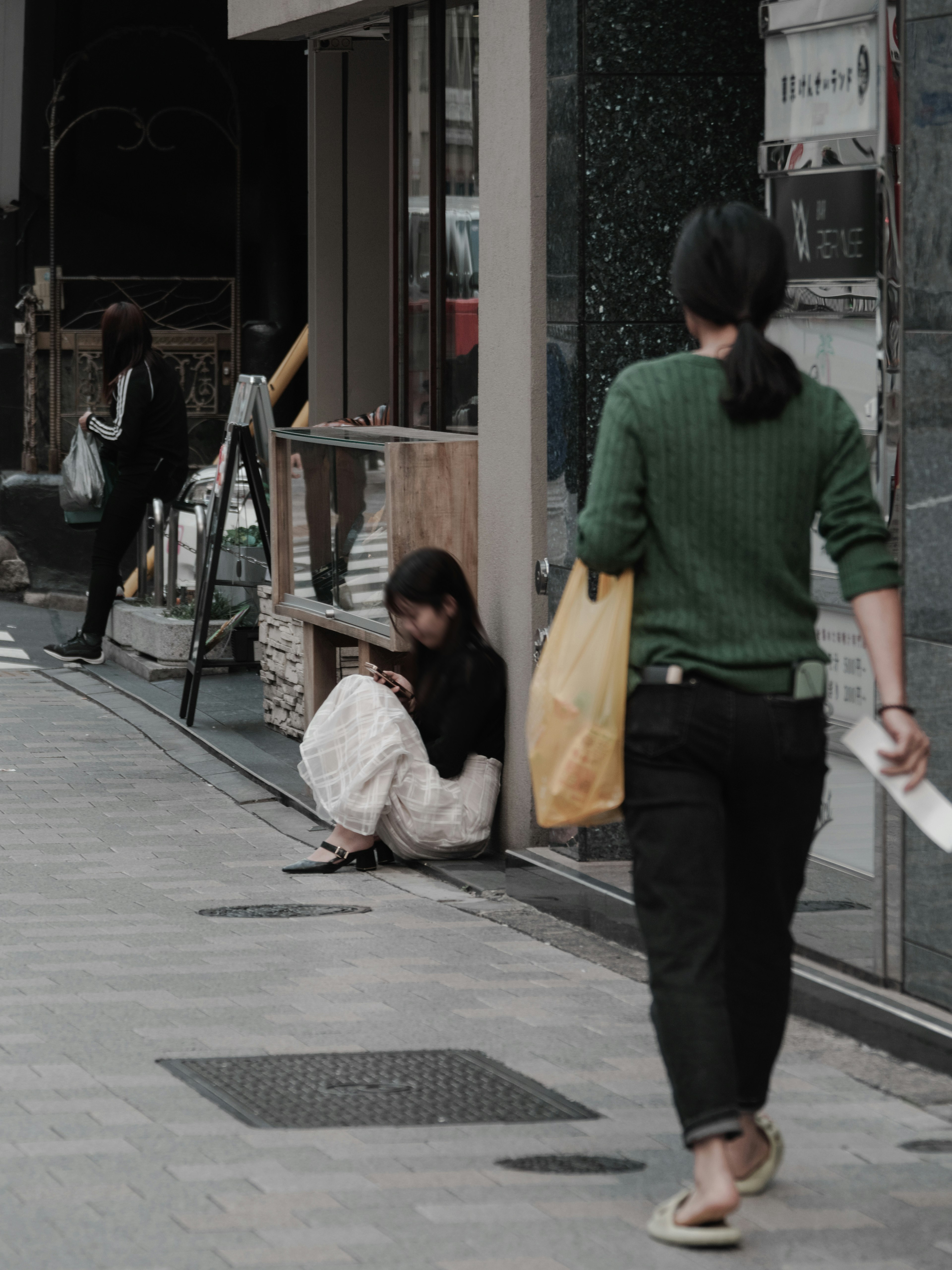 Une scène représentant une femme assise sur le trottoir et une autre femme qui passe