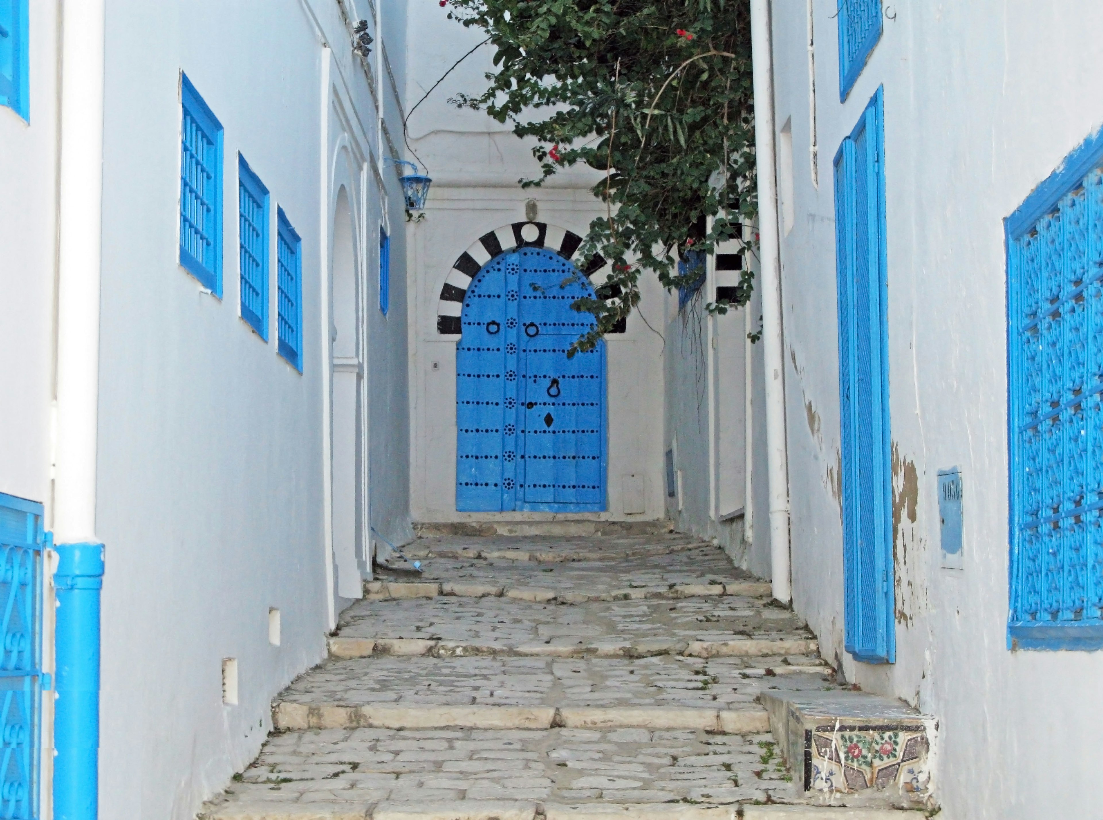 Callejón estrecho con paredes blancas y puerta y ventanas azules