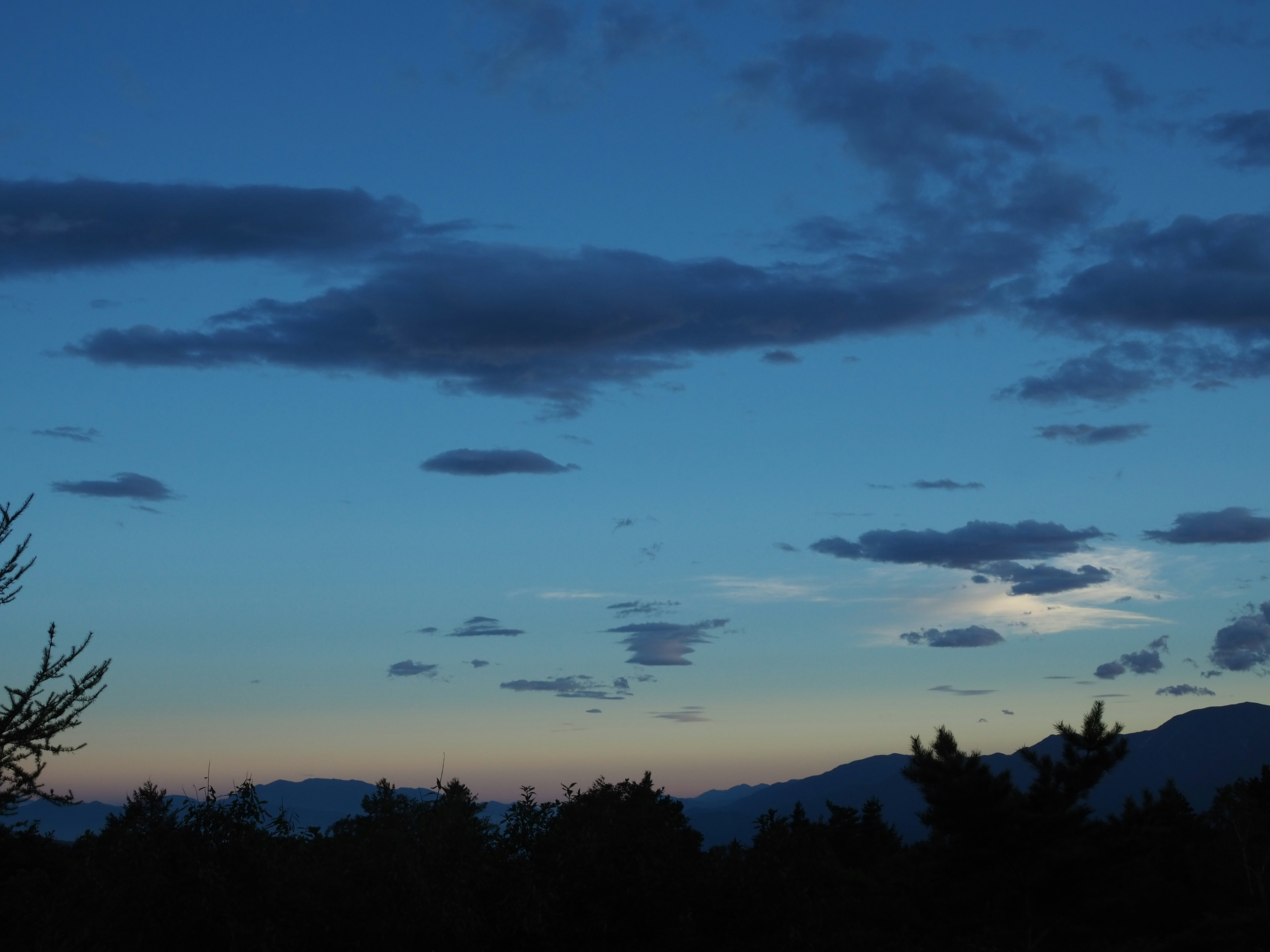 Langit biru dengan awan dan siluet gunung