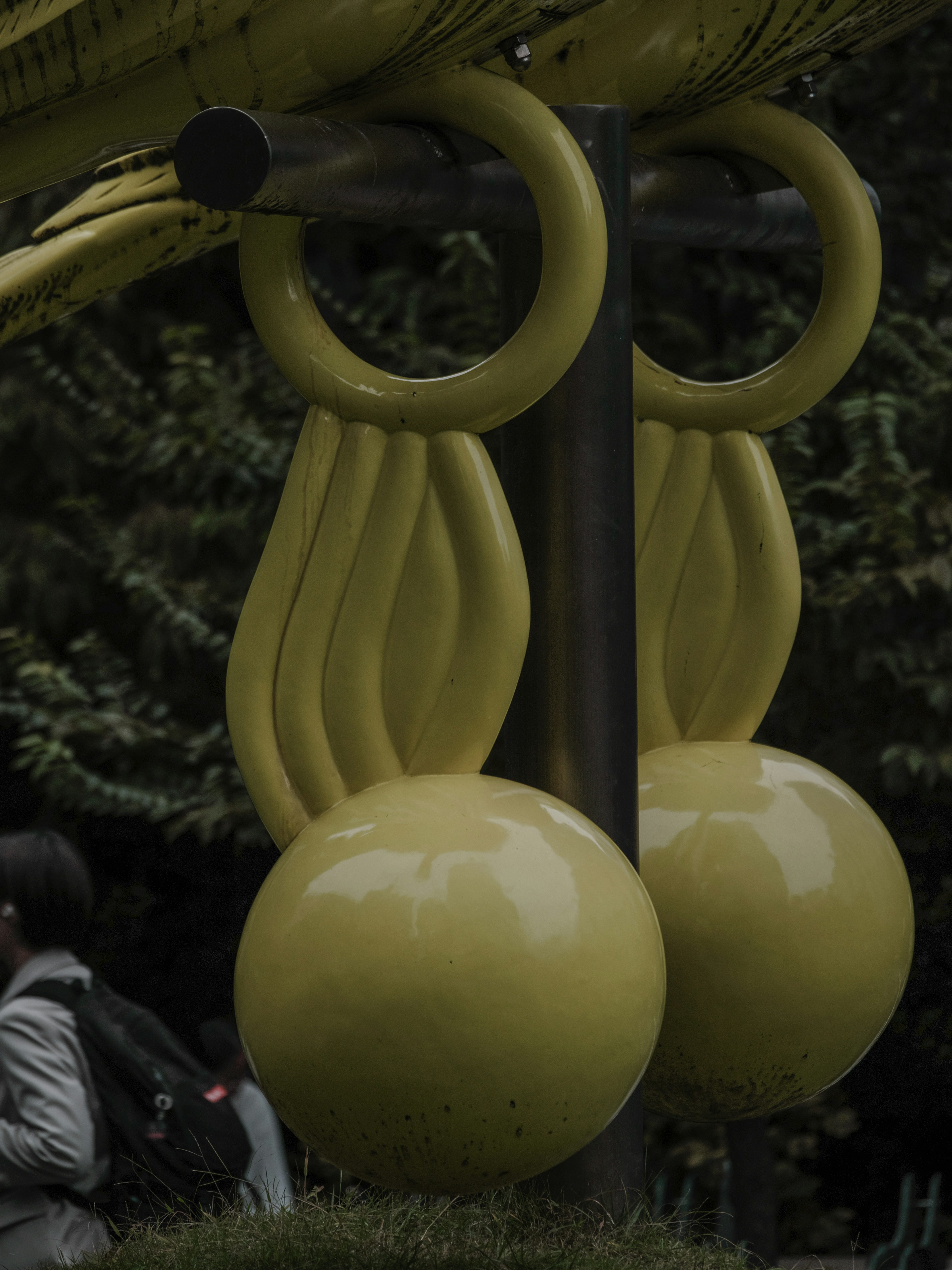 Teil einer gelben Spielplatzstruktur in einem Park mit einem vogelähnlichen Design und runden Kugeln sowie Flügelformen