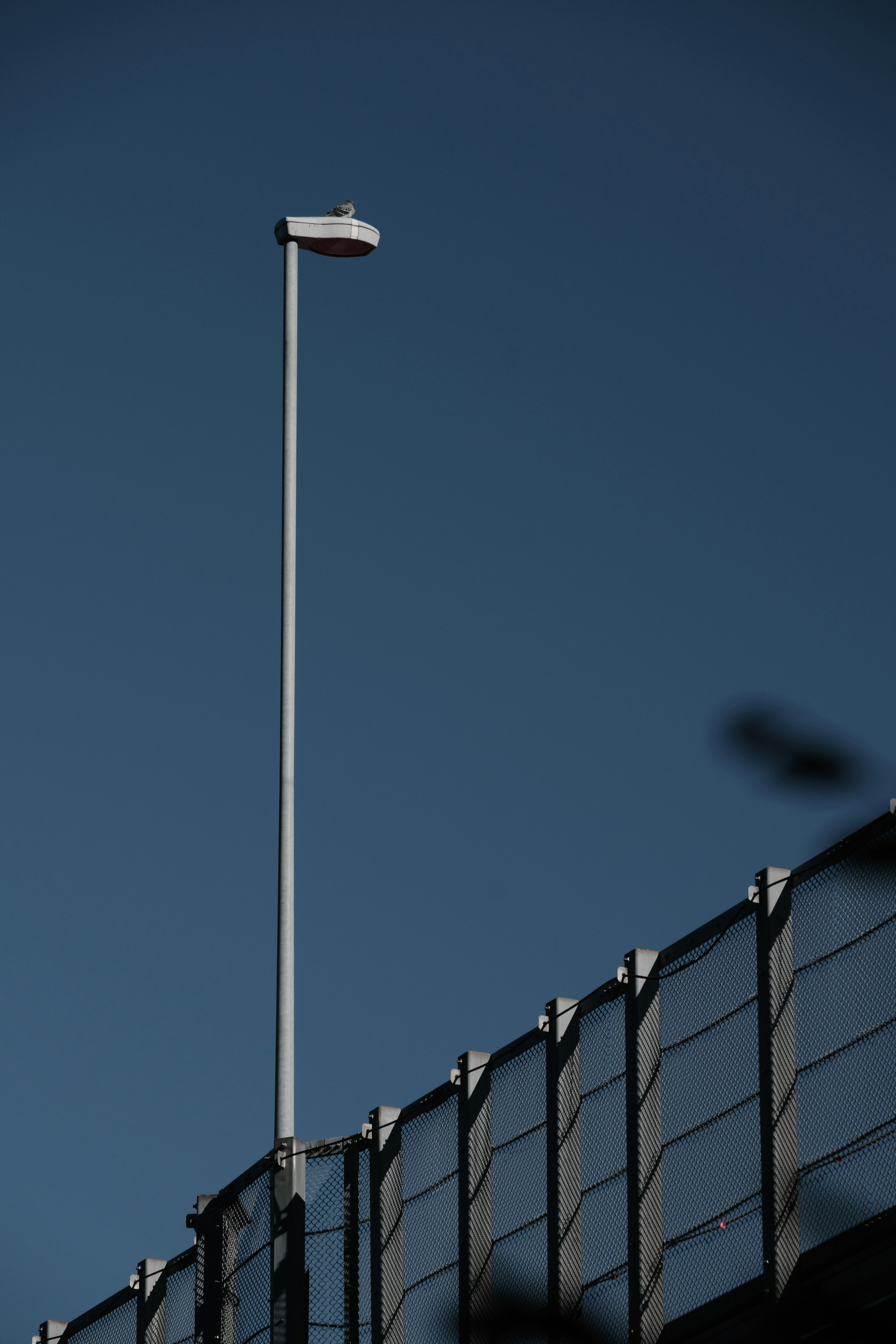 Lampadaire mince sous un ciel bleu avec une clôture en métal en dessous