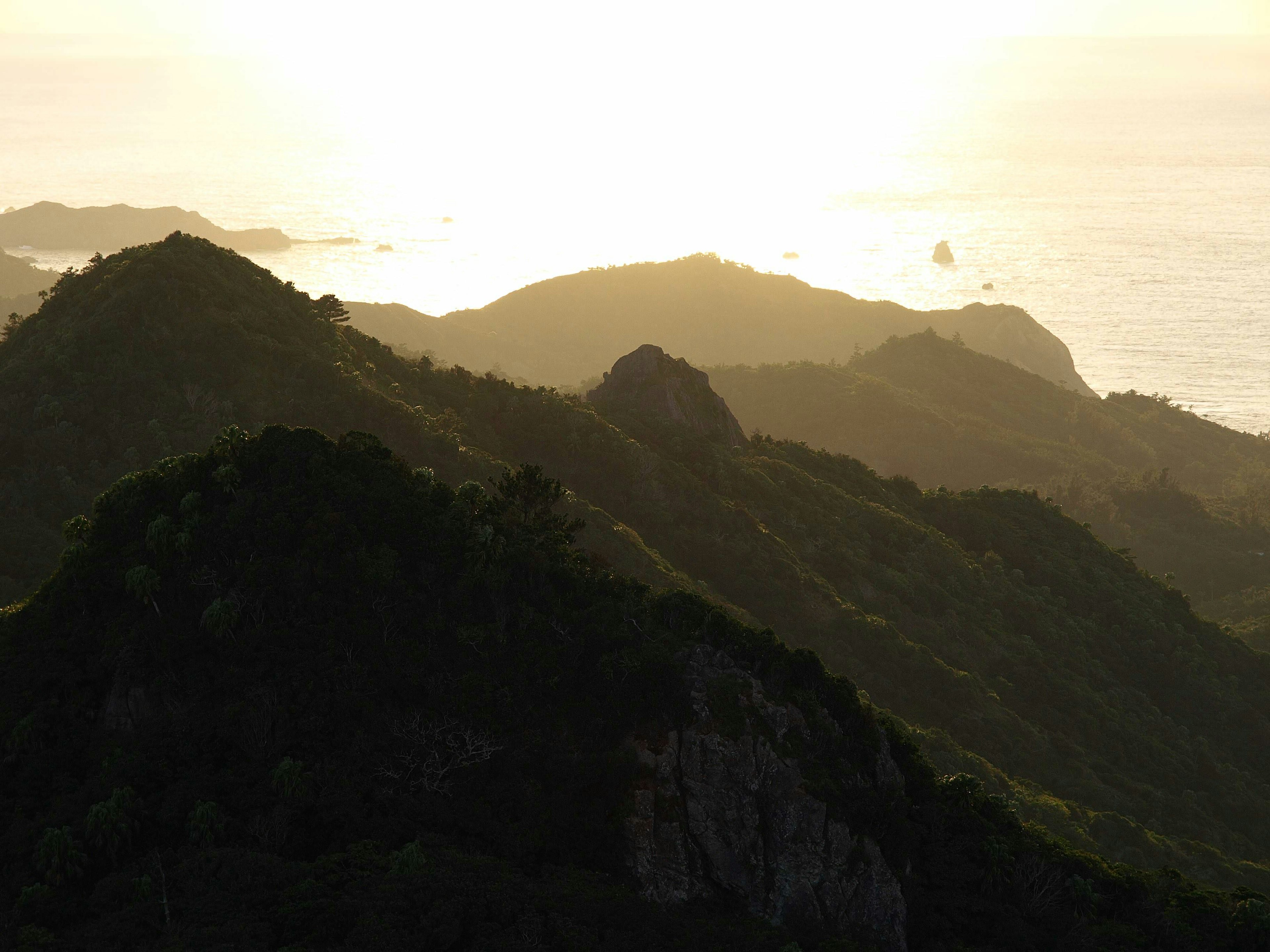 Silhouette of lush green mountains against the backdrop of a sunset over the sea