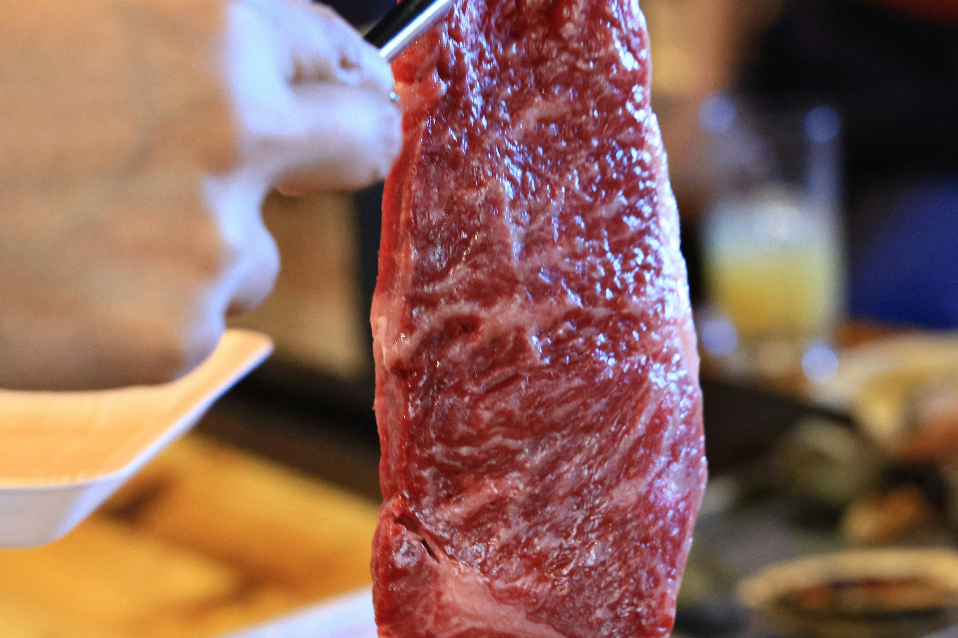 Hand holding a piece of meat with a drink in the background