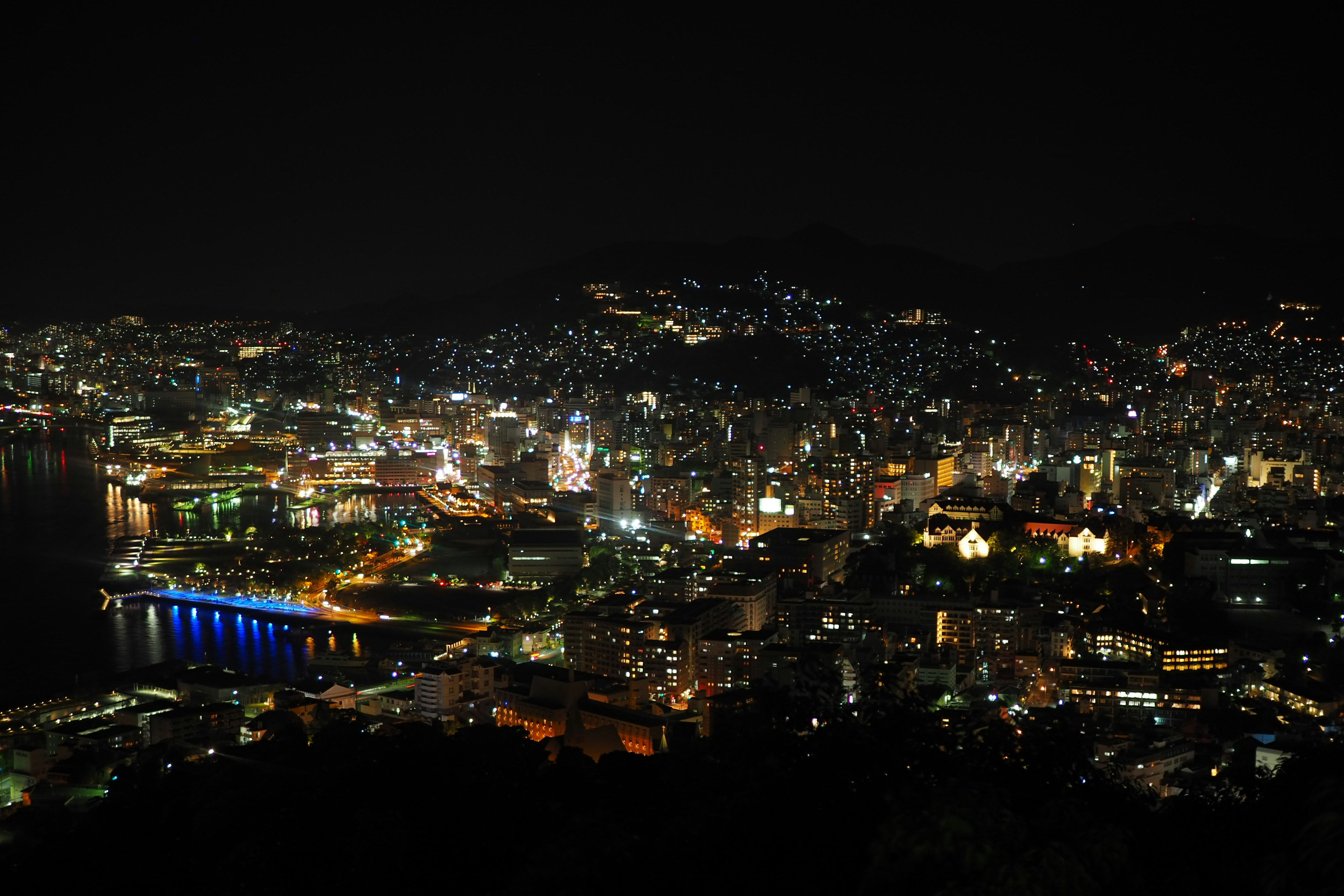 Vista panorámica de la ciudad de Nagasaki de noche con luces brillantes y reflejos en el agua