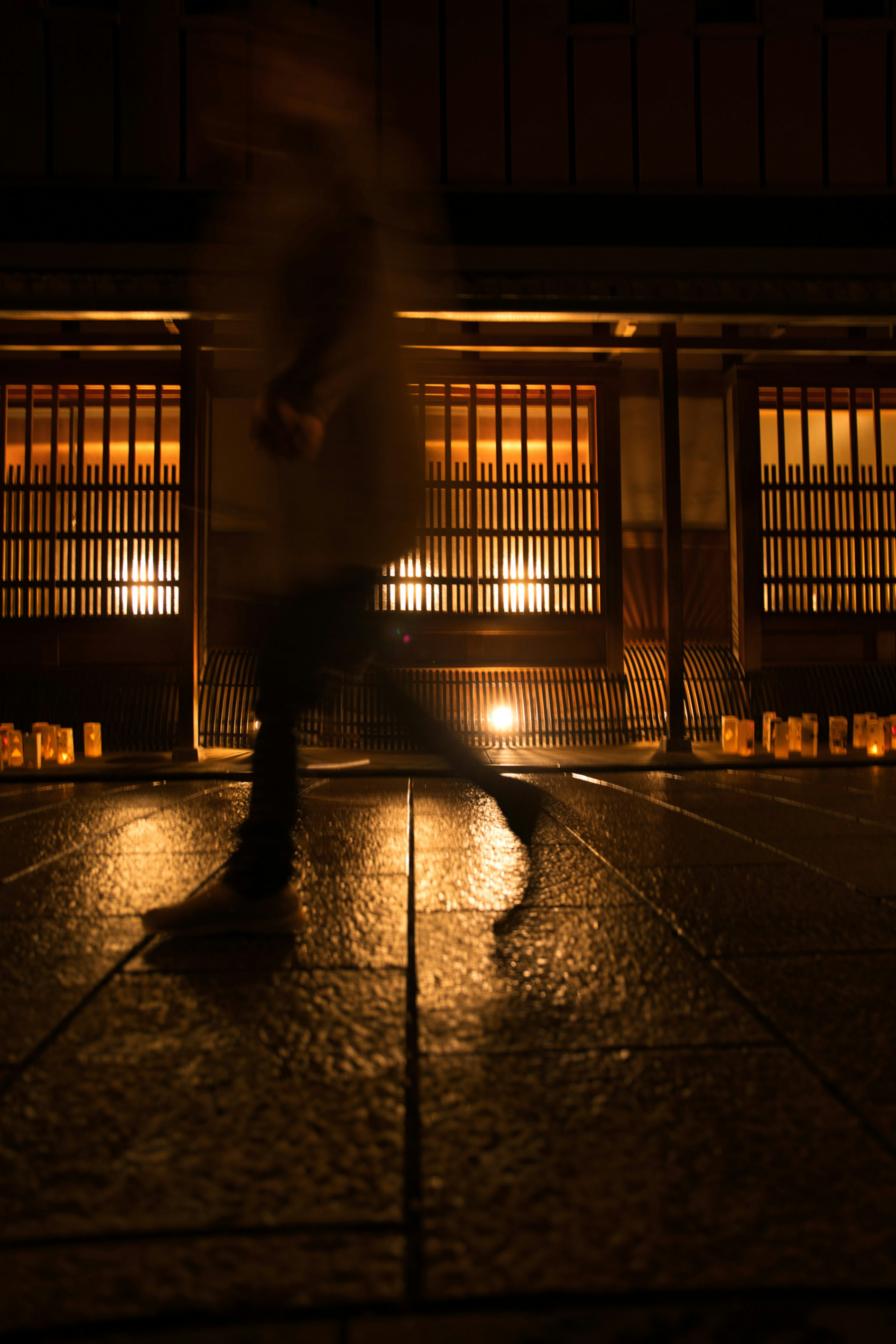 Silhouette di una persona che cammina in una strada poco illuminata con luci calde provenienti dagli edifici