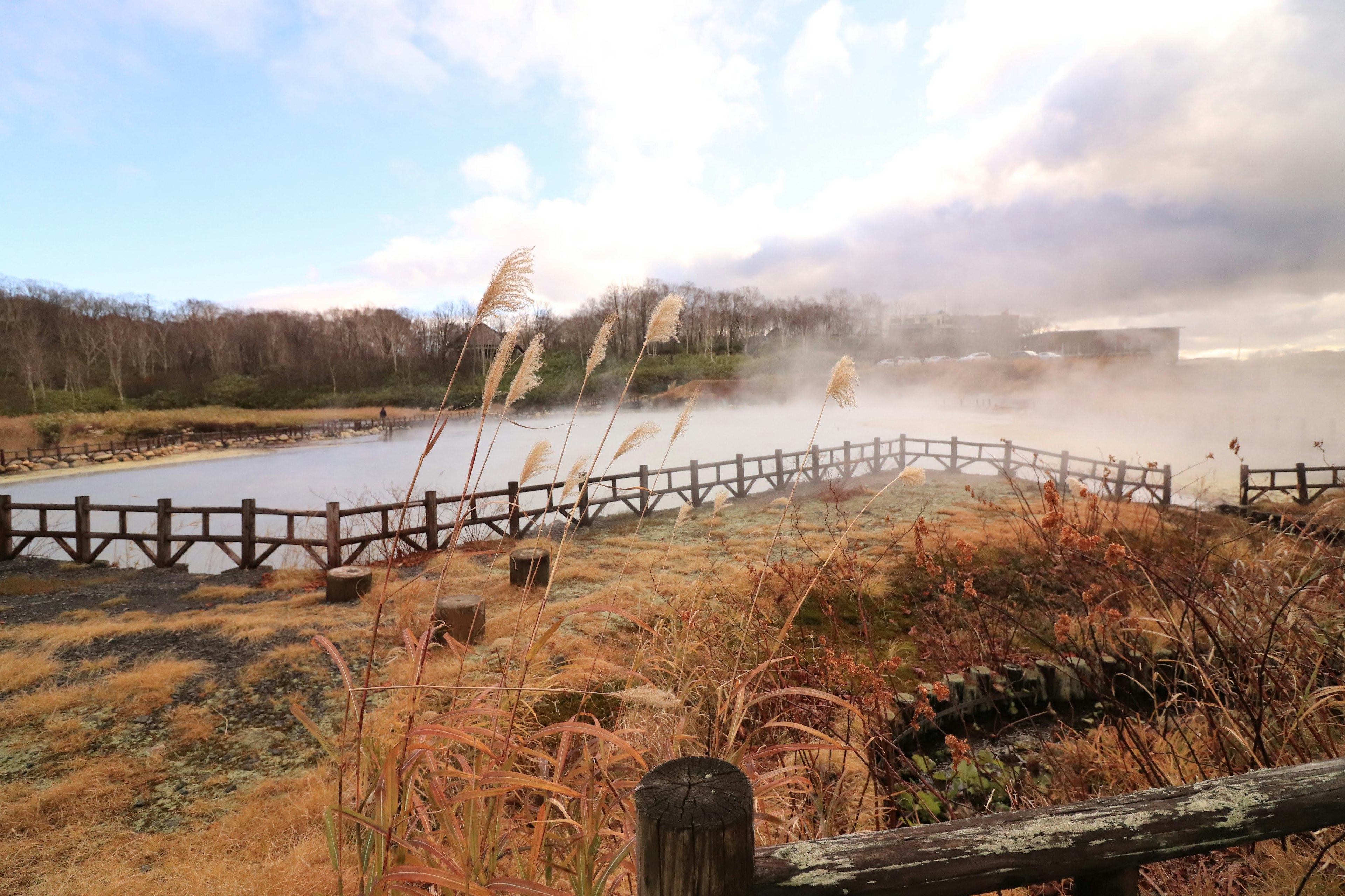 Vue panoramique d'un lac calme avec de la vapeur s'élevant des sources chaudes clôture en bois et prairie sèche