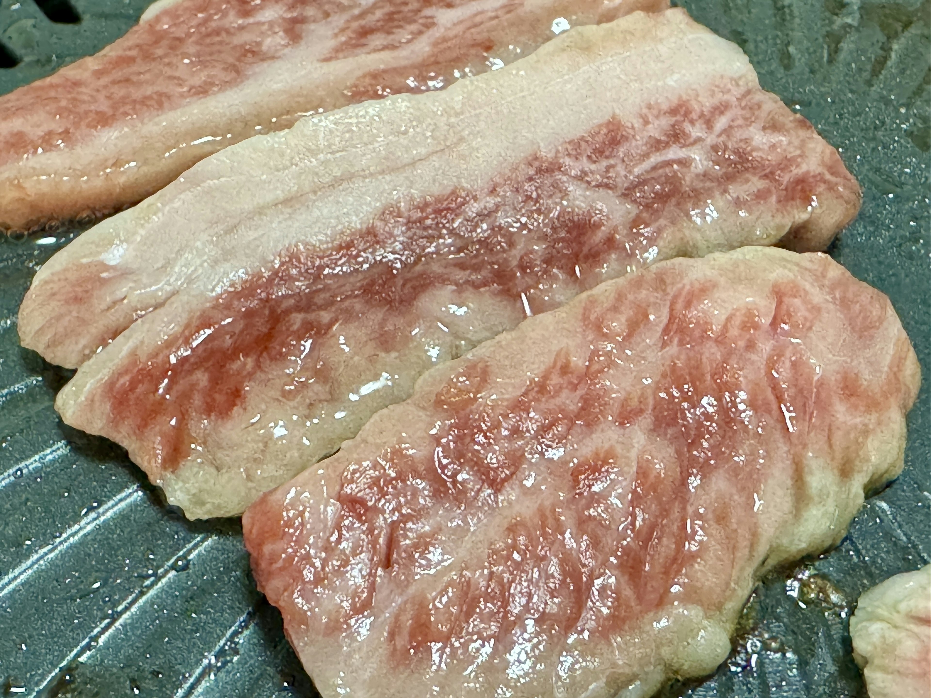 Slices of marbled meat grilling on a plate