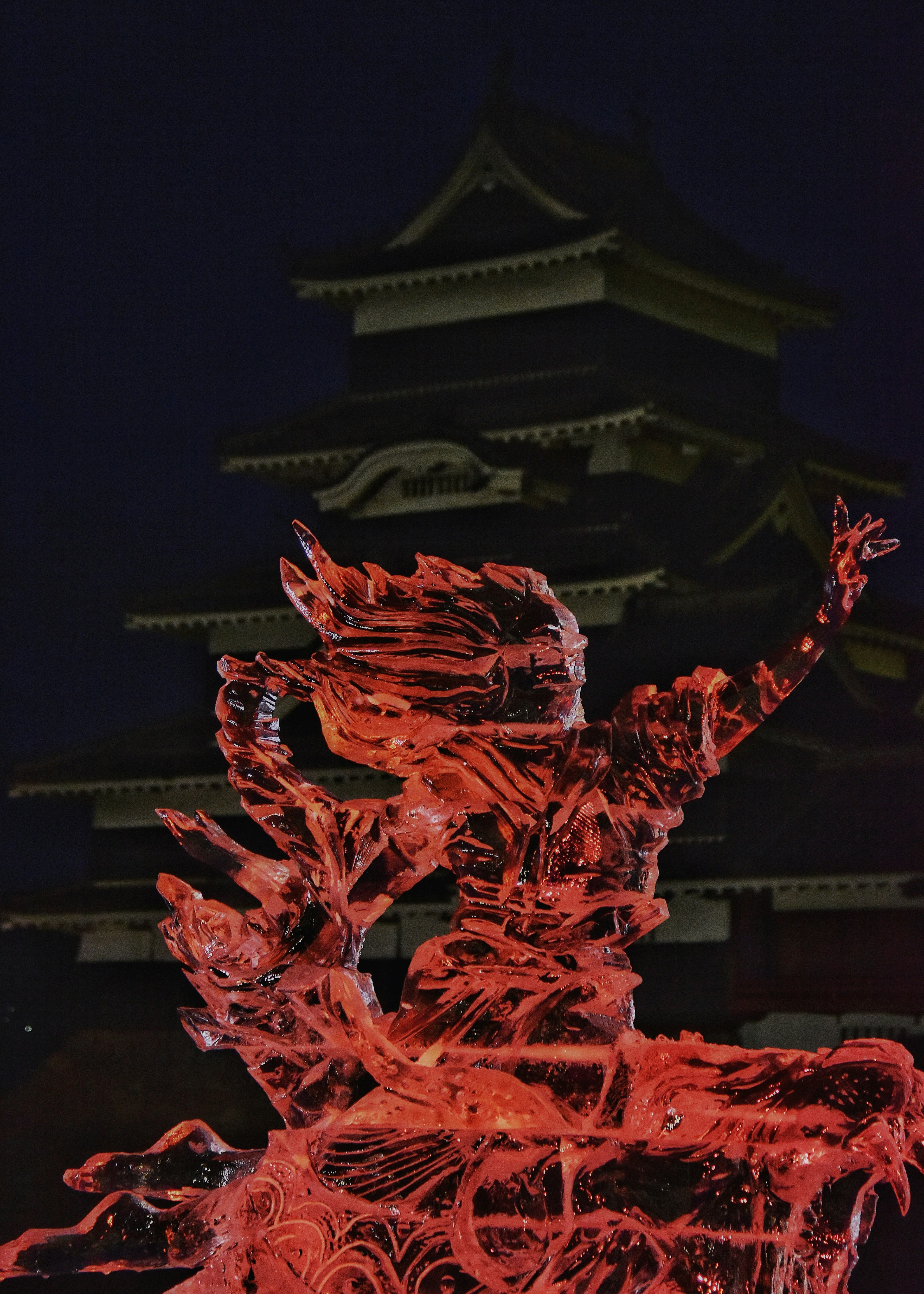 Une sculpture de glace rouge au premier plan avec une architecture japonaise traditionnelle en arrière-plan la nuit