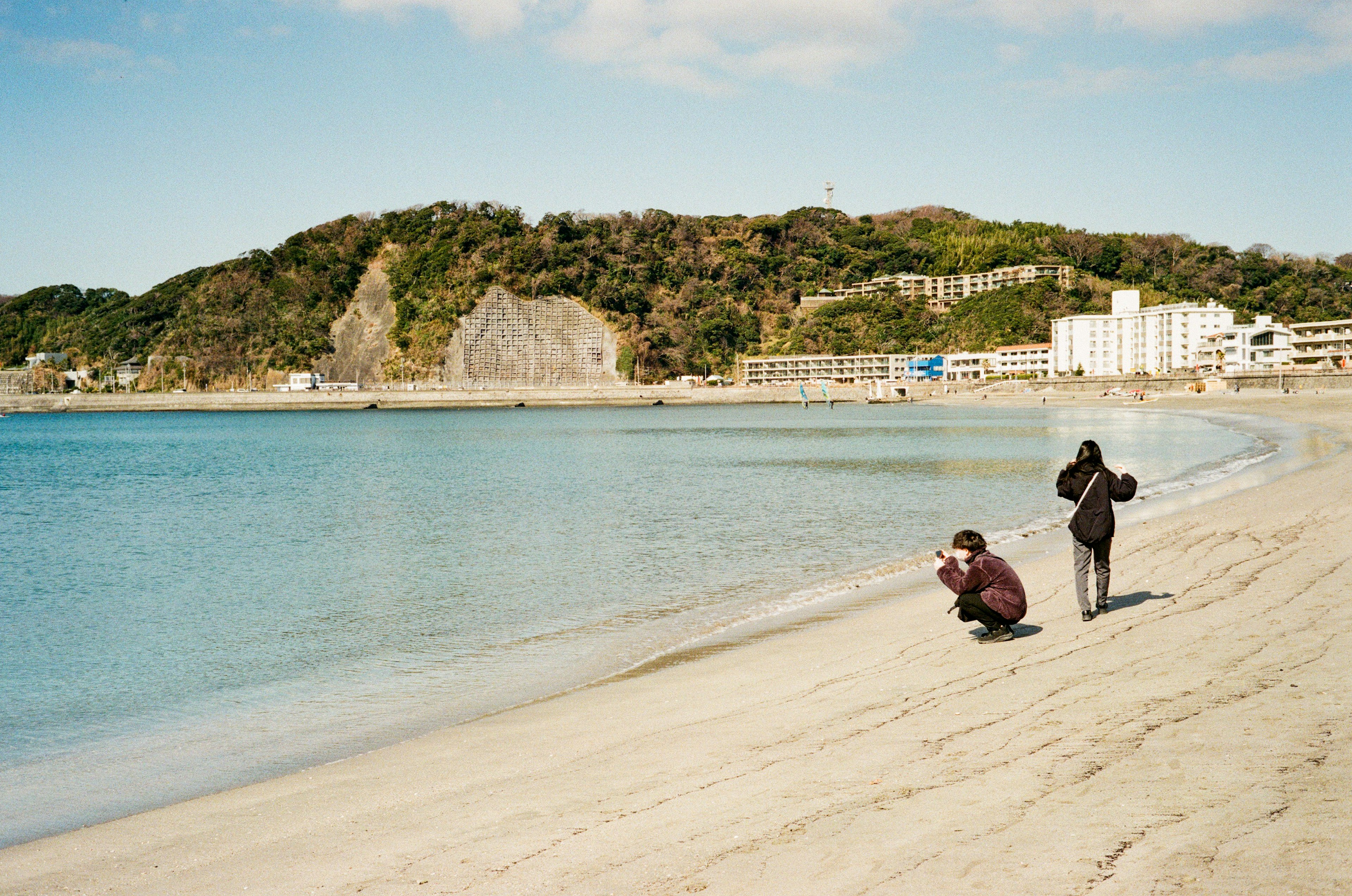 Two people taking photos on a beach with a scenic backdrop