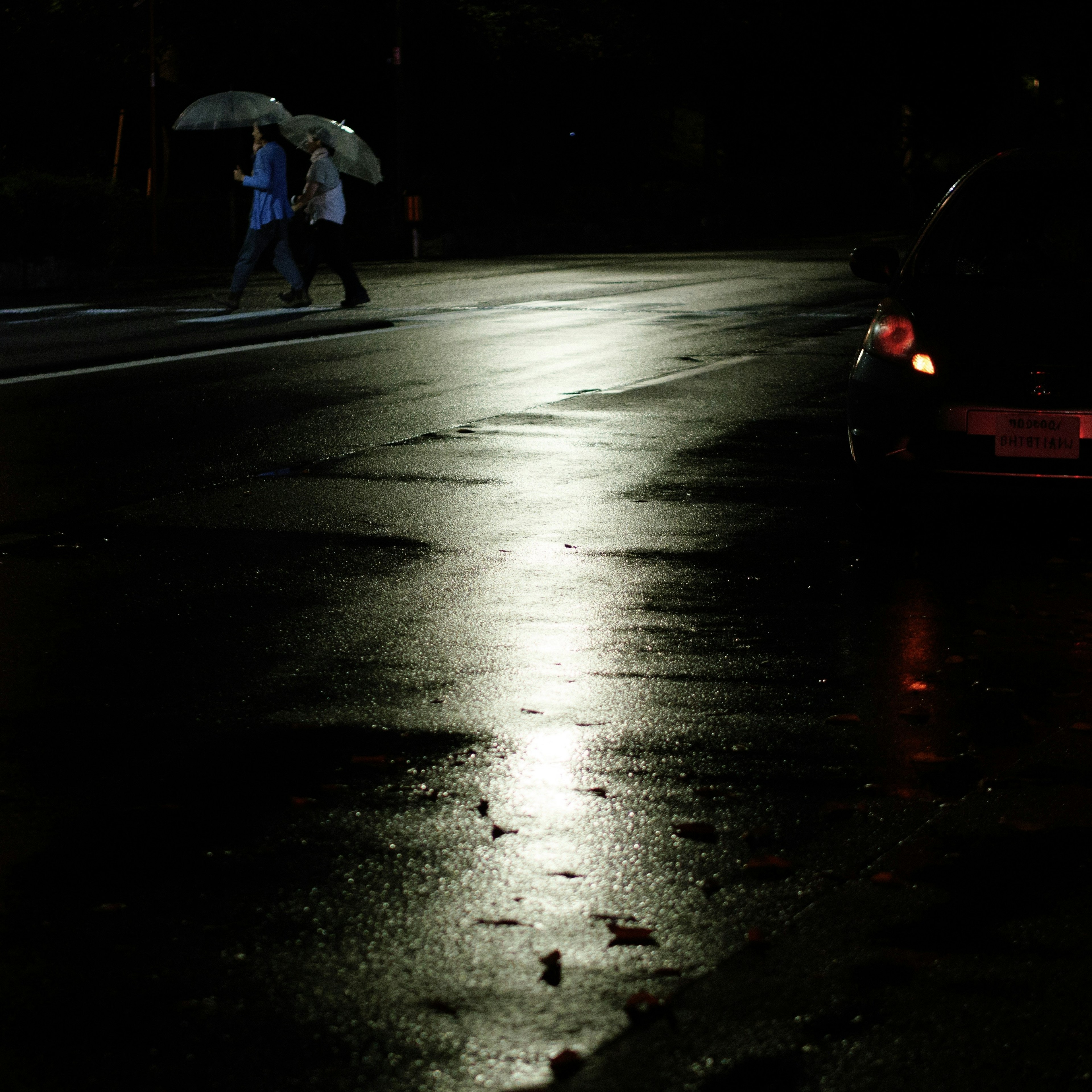 雨の中、傘を持った二人が暗い通りを歩いている