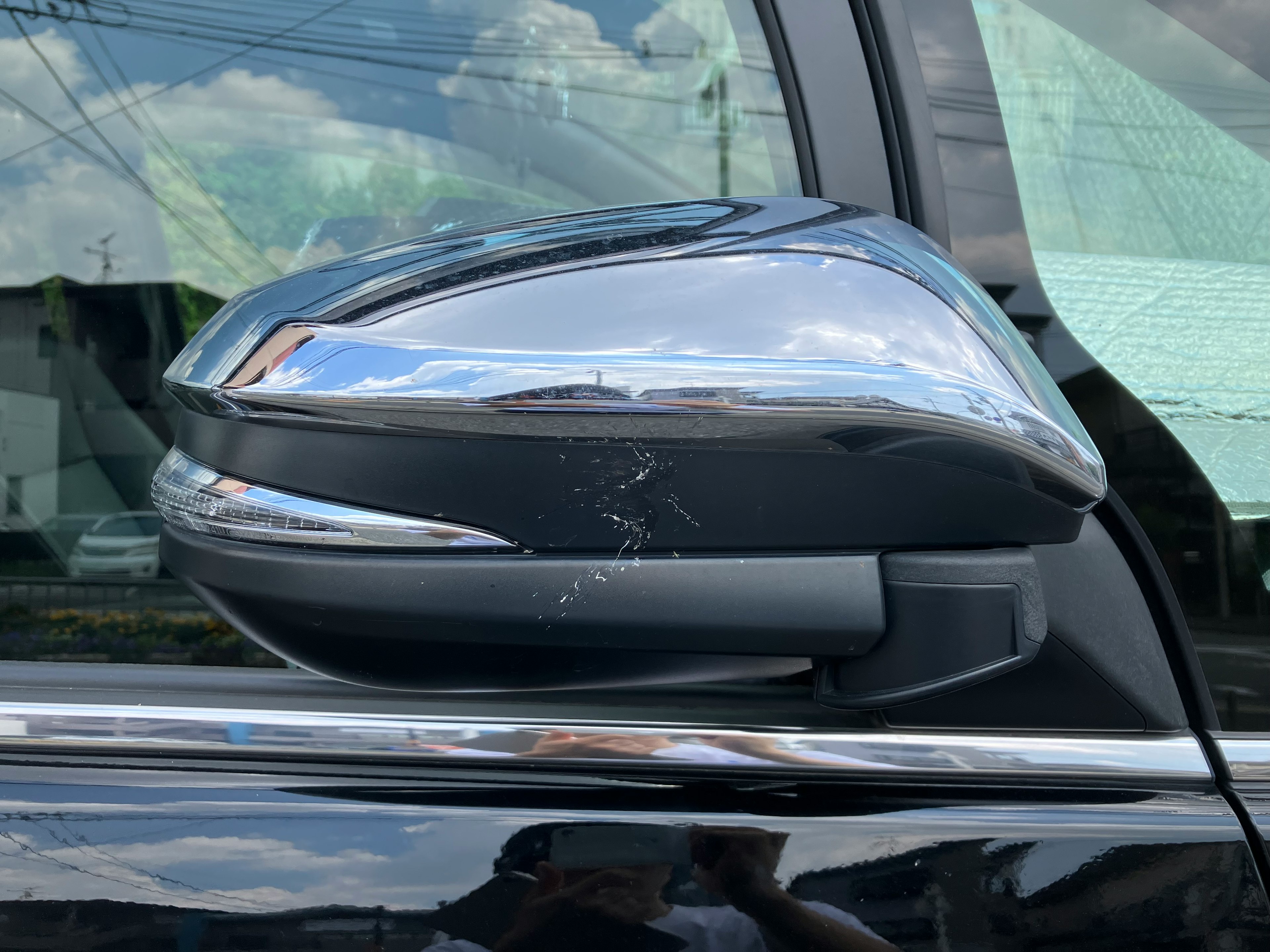 Close-up of a black car's side mirror with a scratch on the reflective surface