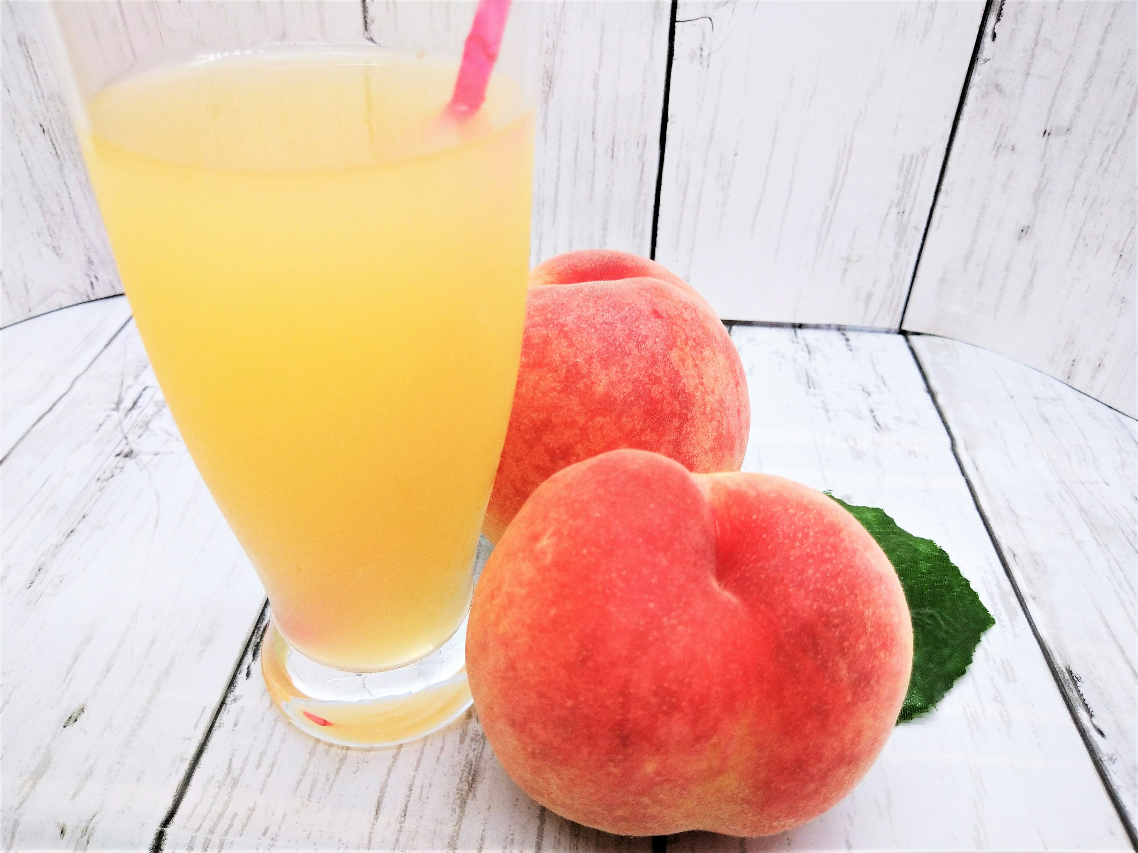 A glass of peach juice with fresh peaches beside it