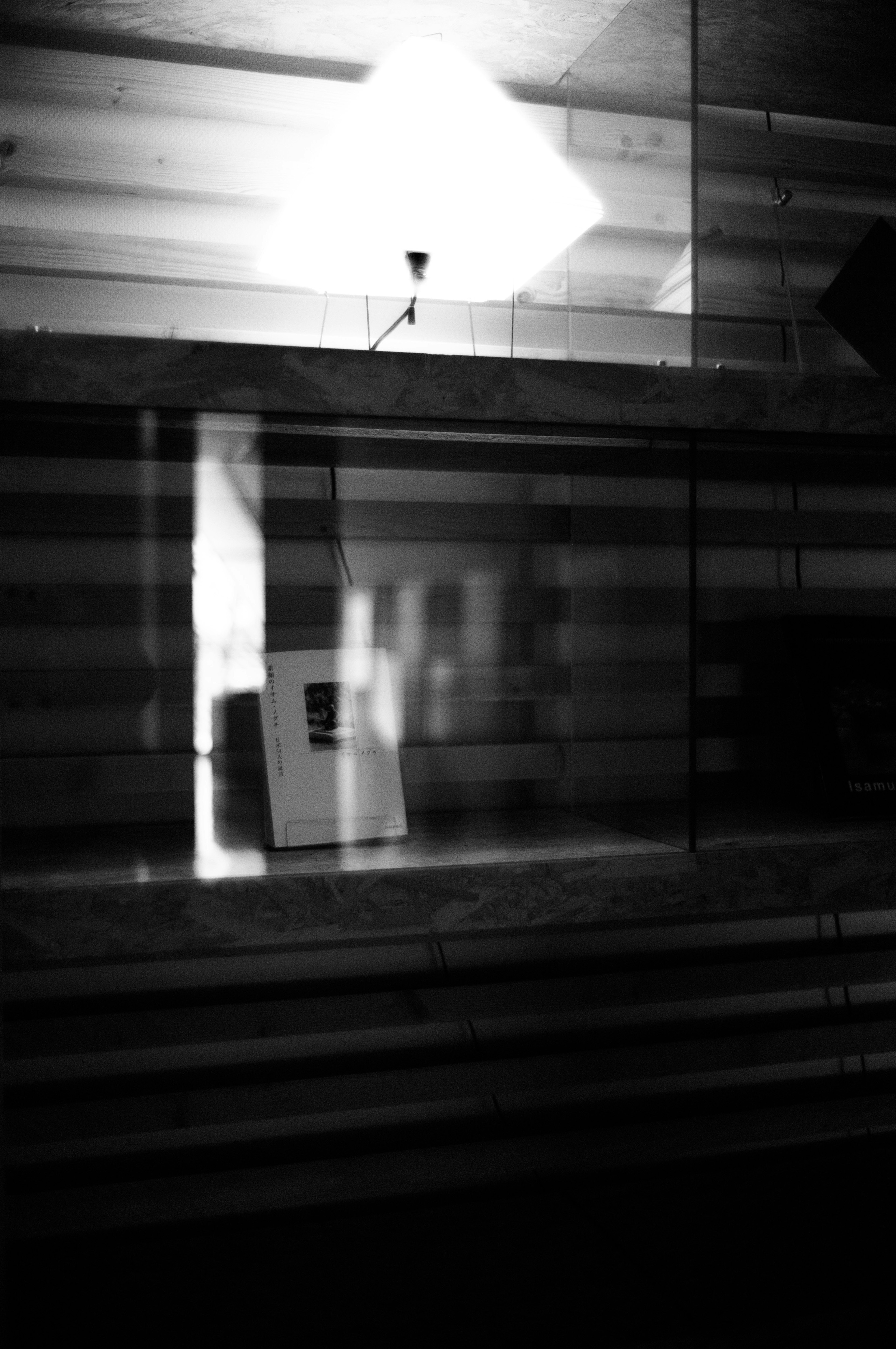 Black and white image showing light and shadows through a window with interior lighting and furniture silhouettes