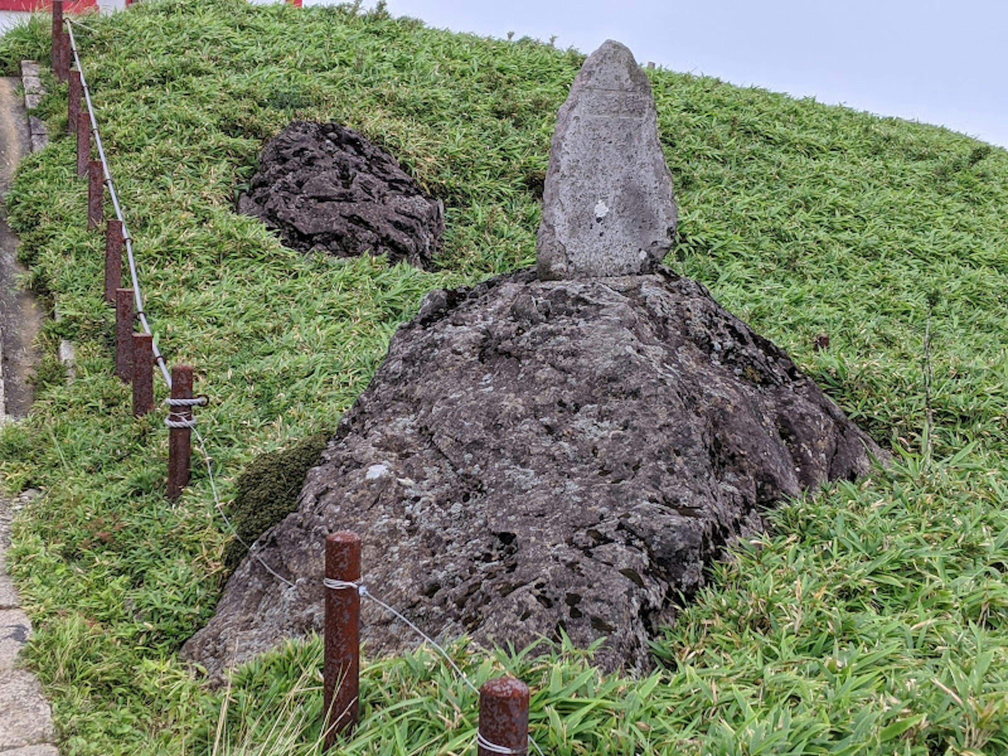 Landschaft mit einem Steindenkmal umgeben von Gras und einem Erdhügel