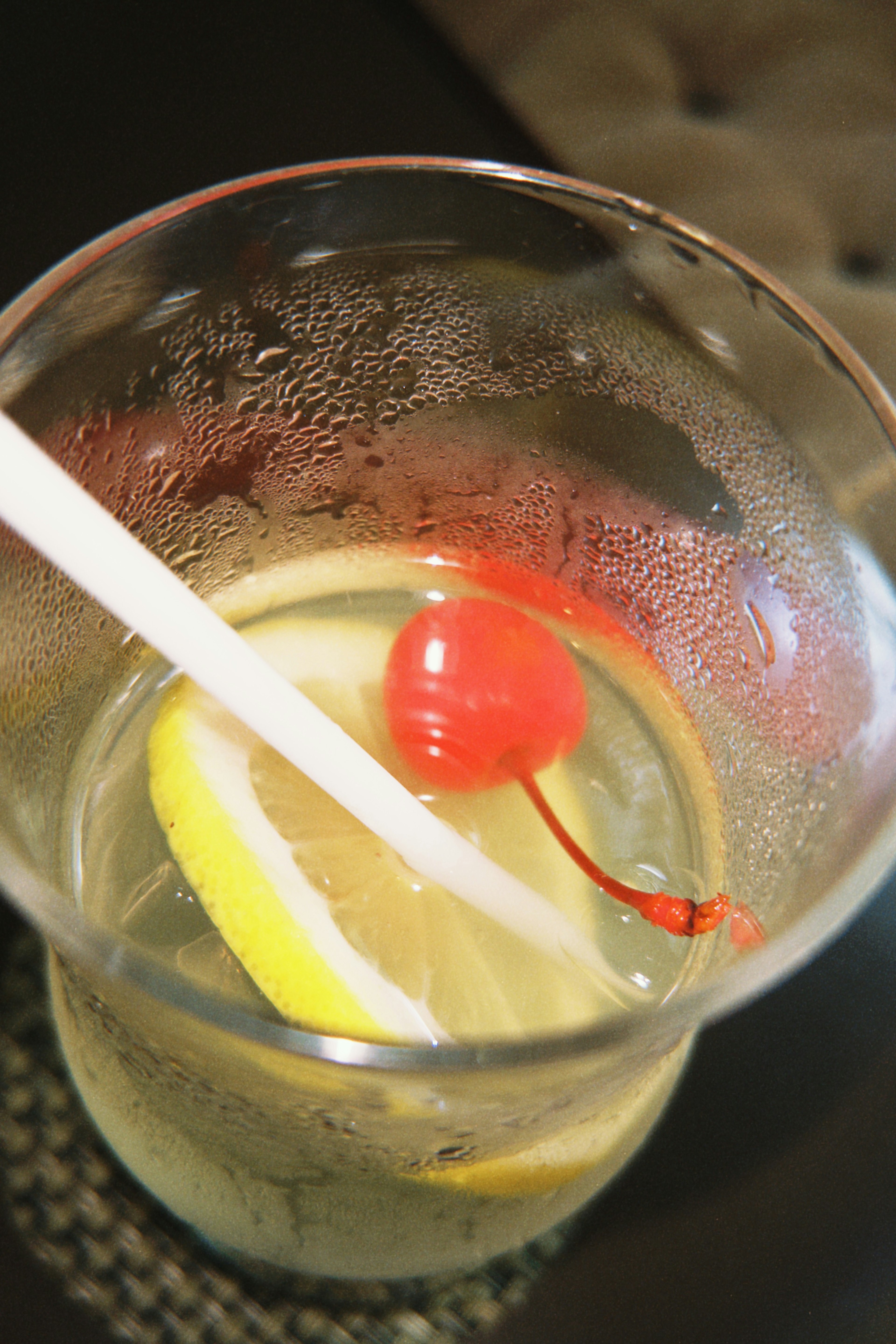 Cocktail in a clear glass with ice, lemon slices, and a cherry