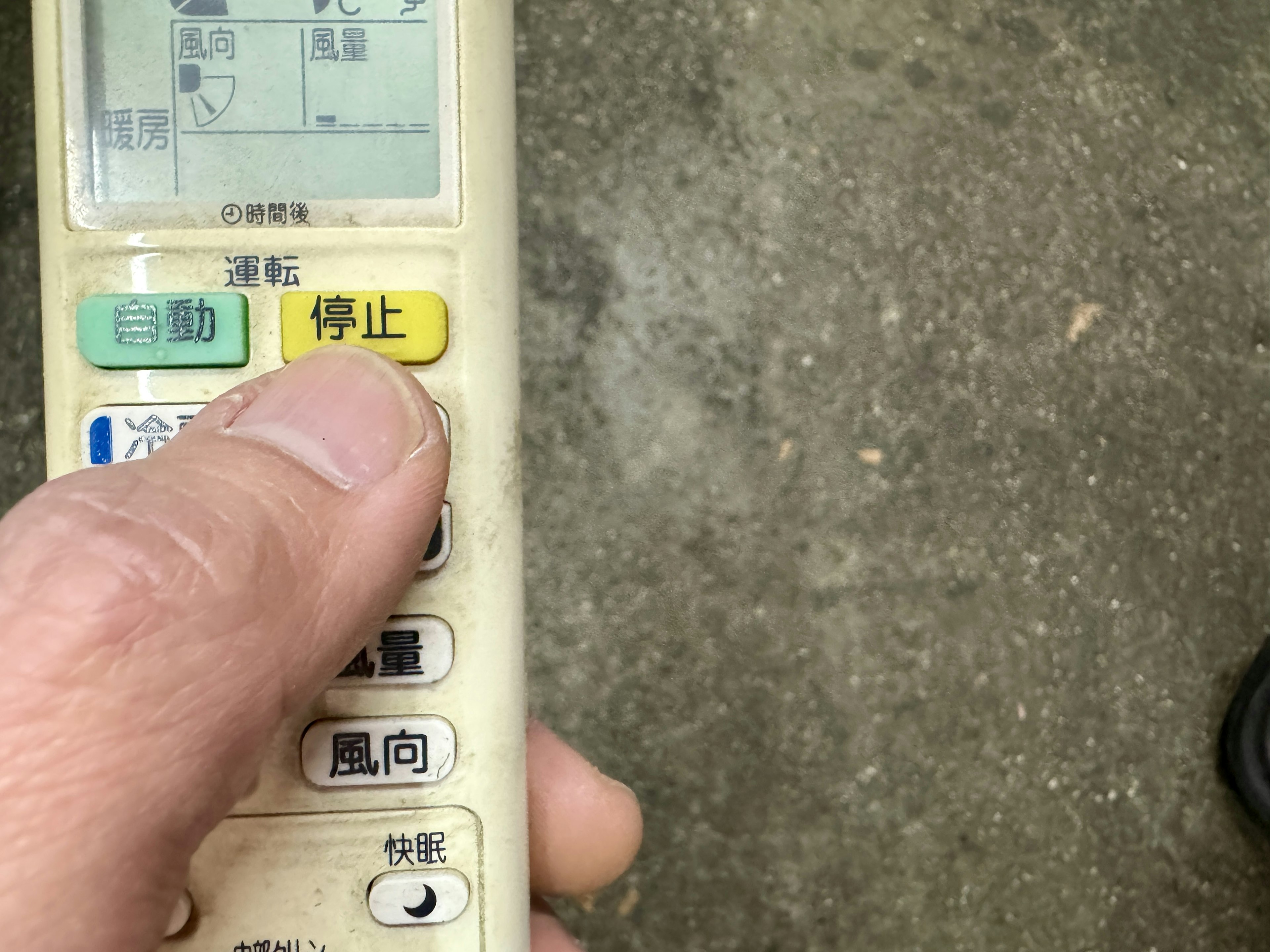 A hand holding an air conditioning remote control over a concrete surface